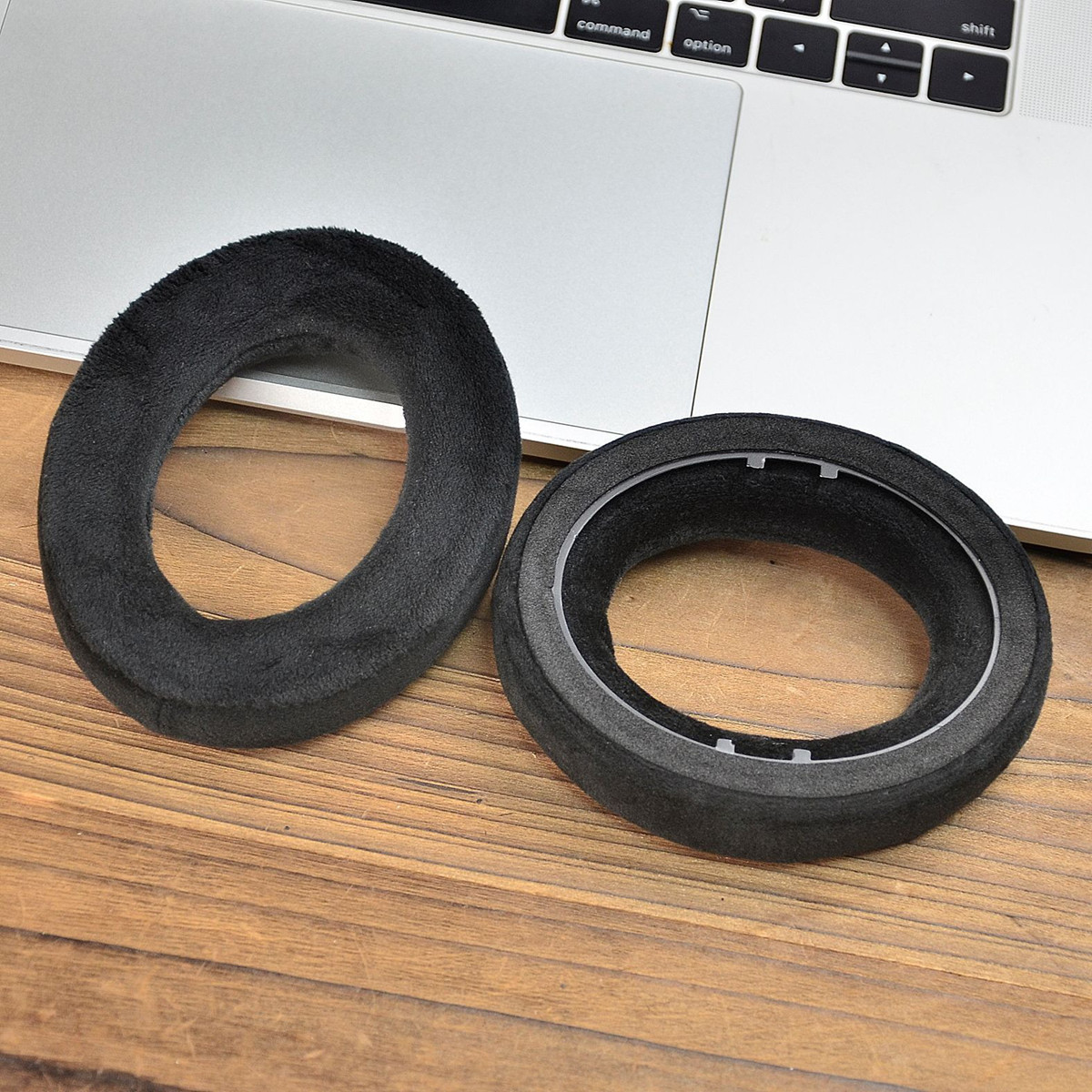Due cuscinetti auricolari neri per cuffie su un tavolo di legno. Uno è intatto, l'altro è solo il telaio.