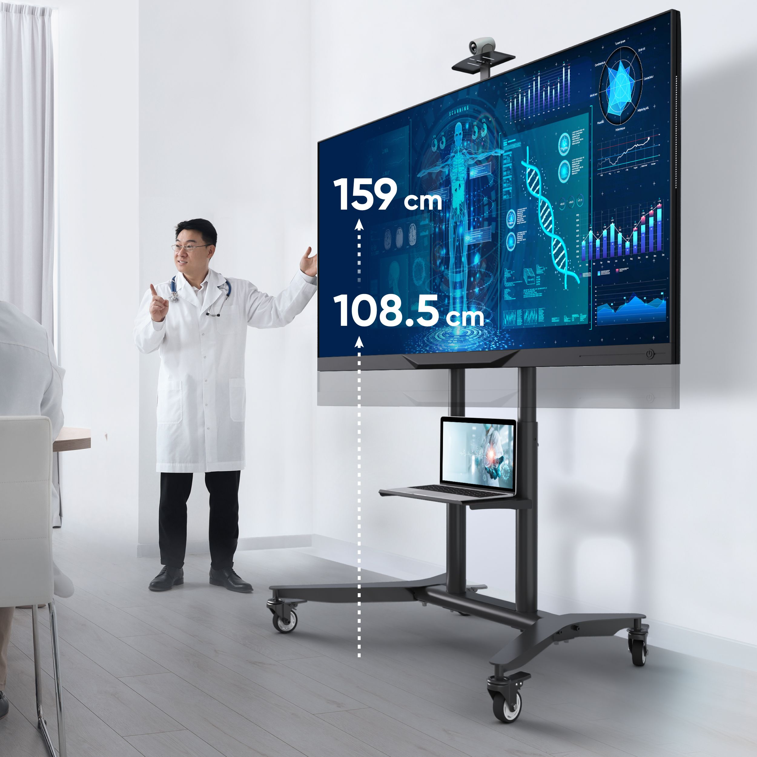 Lekarz wskazuje na ekran z danymi medycznymi, na stojaku na kółkach z laptopem i kamerą.