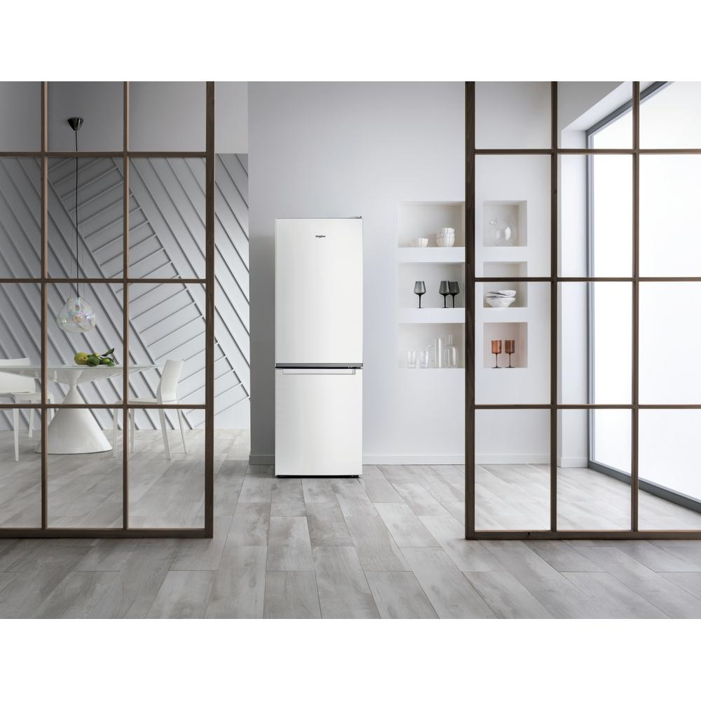 Un frigorifero bianco in una stanza moderna. La stanza ha pareti di vetro, pavimenti in legno e un tavolo e sedie visibili.