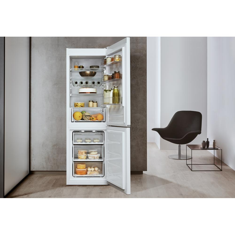Frigorifero bianco con porta aperta, rivela ripiani e contenuto. Sedia e tavolo neri a destra.
