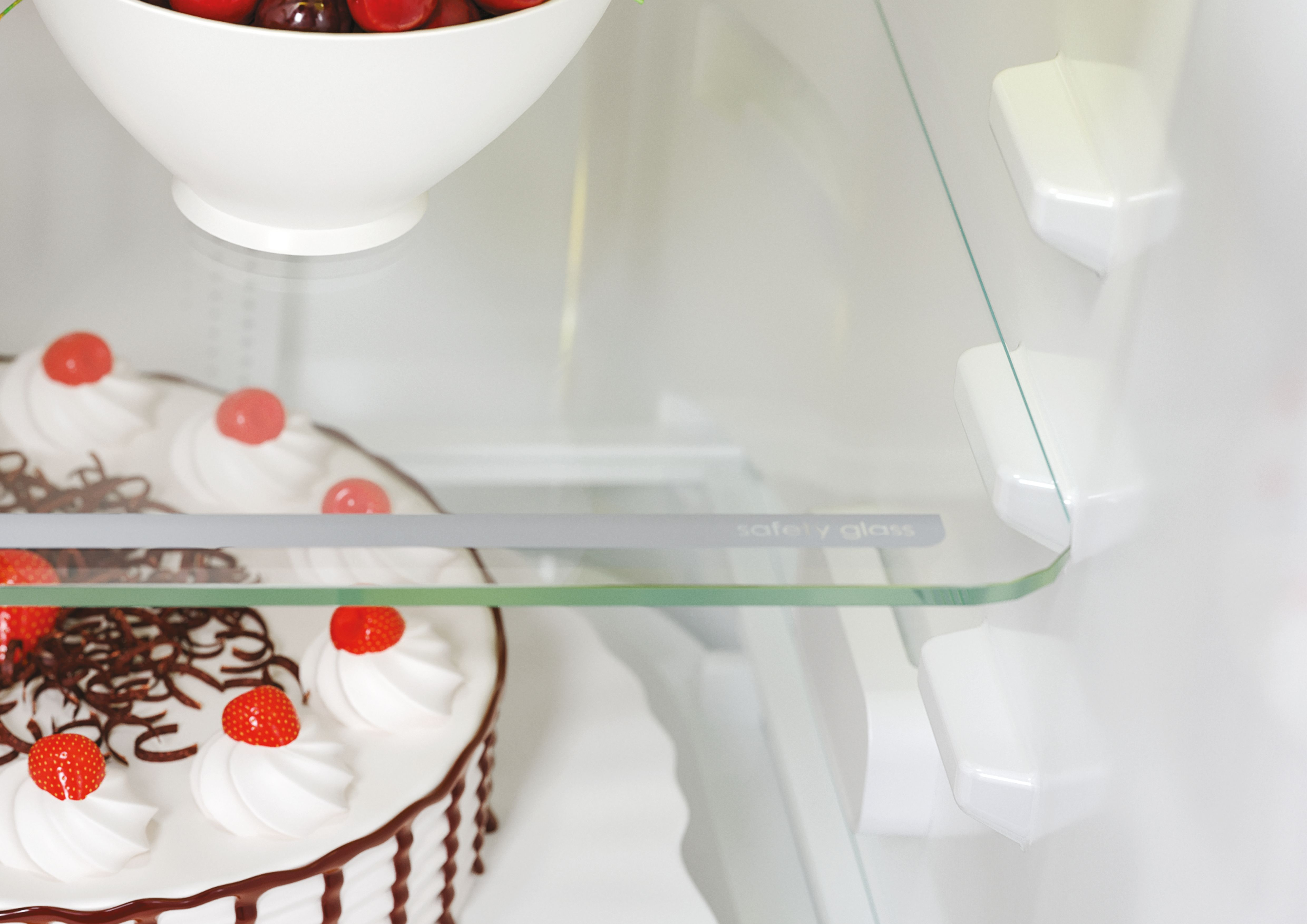 Primo piano di una torta con ciliegie su un ripiano di vetro all'interno di un frigorifero, con etichetta 'safety glass'.
