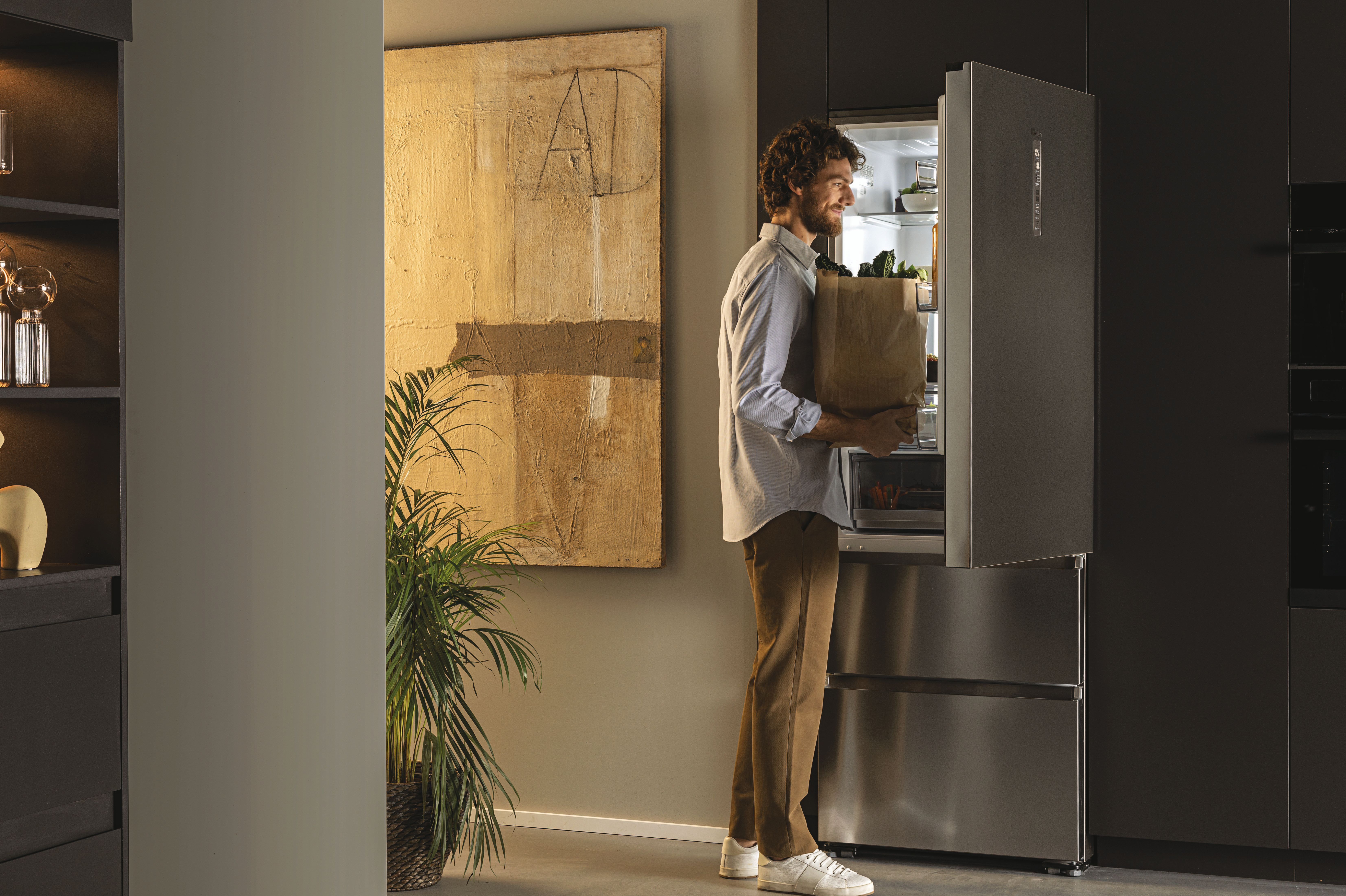 Un hombre con una bolsa de papel se para frente a un refrigerador Haier en una cocina moderna.