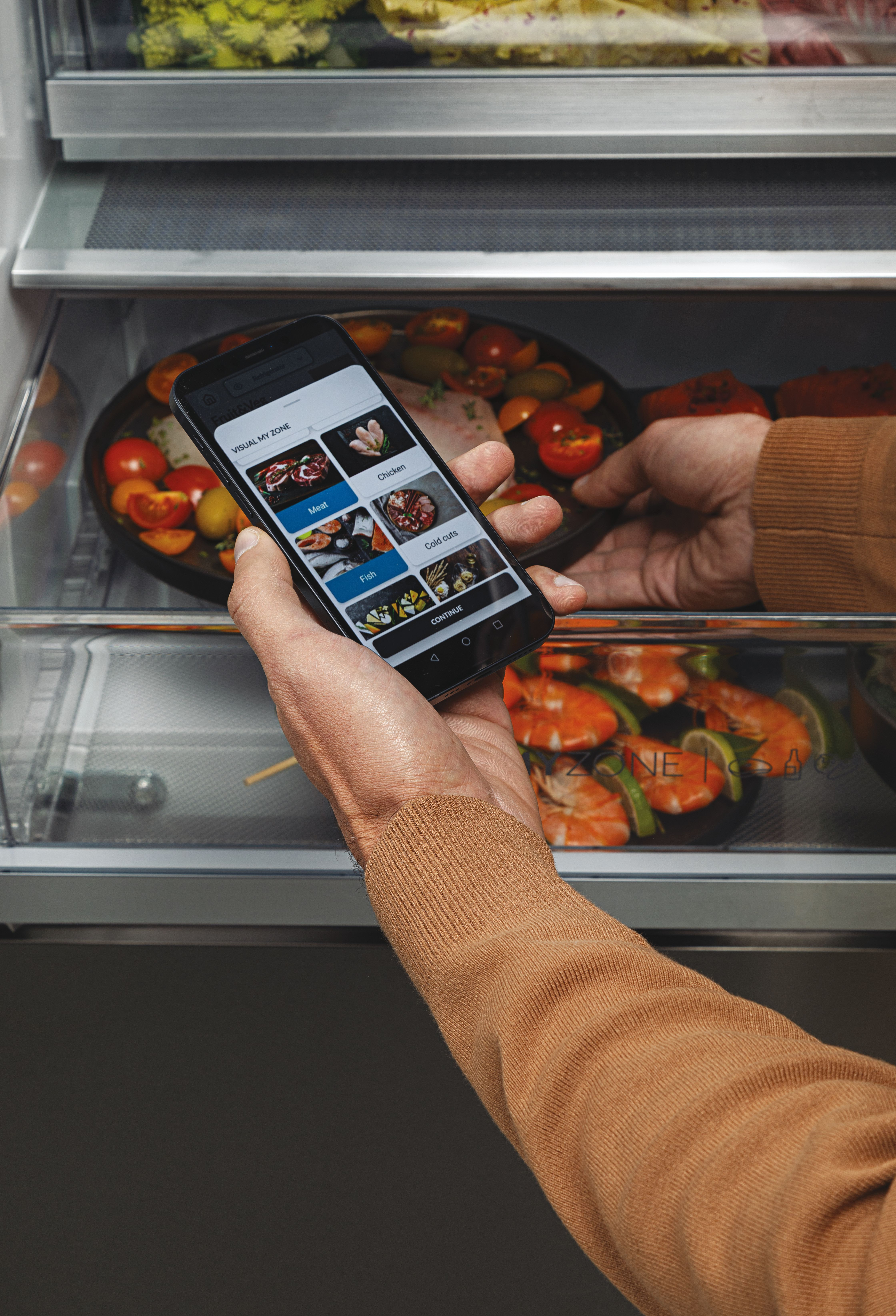 Vista de cerca de la mano de una persona sosteniendo un teléfono cerca del contenido del refrigerador. El teléfono muestra opciones de comida.