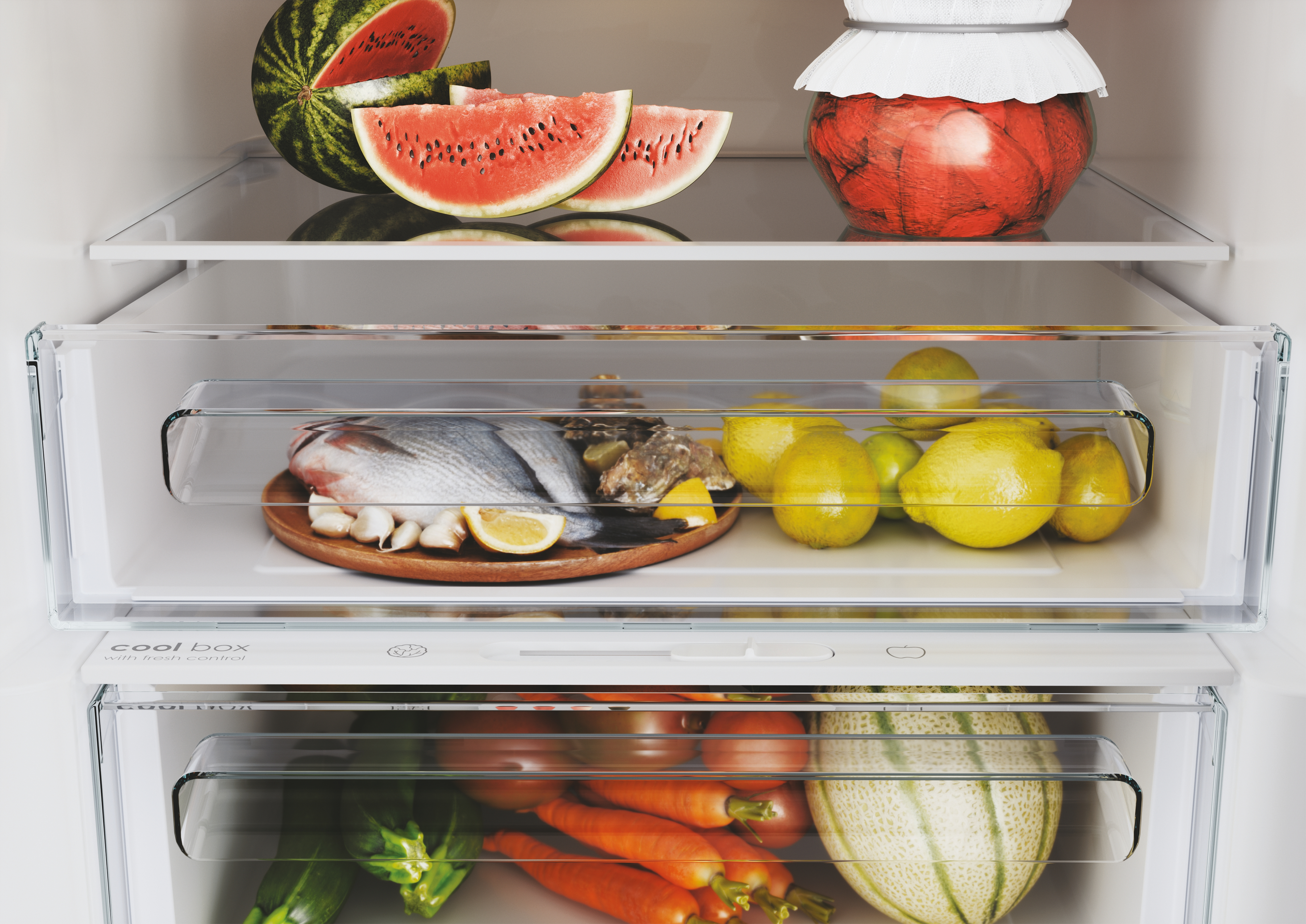 Wewnątrz lodówki wystawione są arbuzy, ryby, cytryny i inne owoce i warzywa.