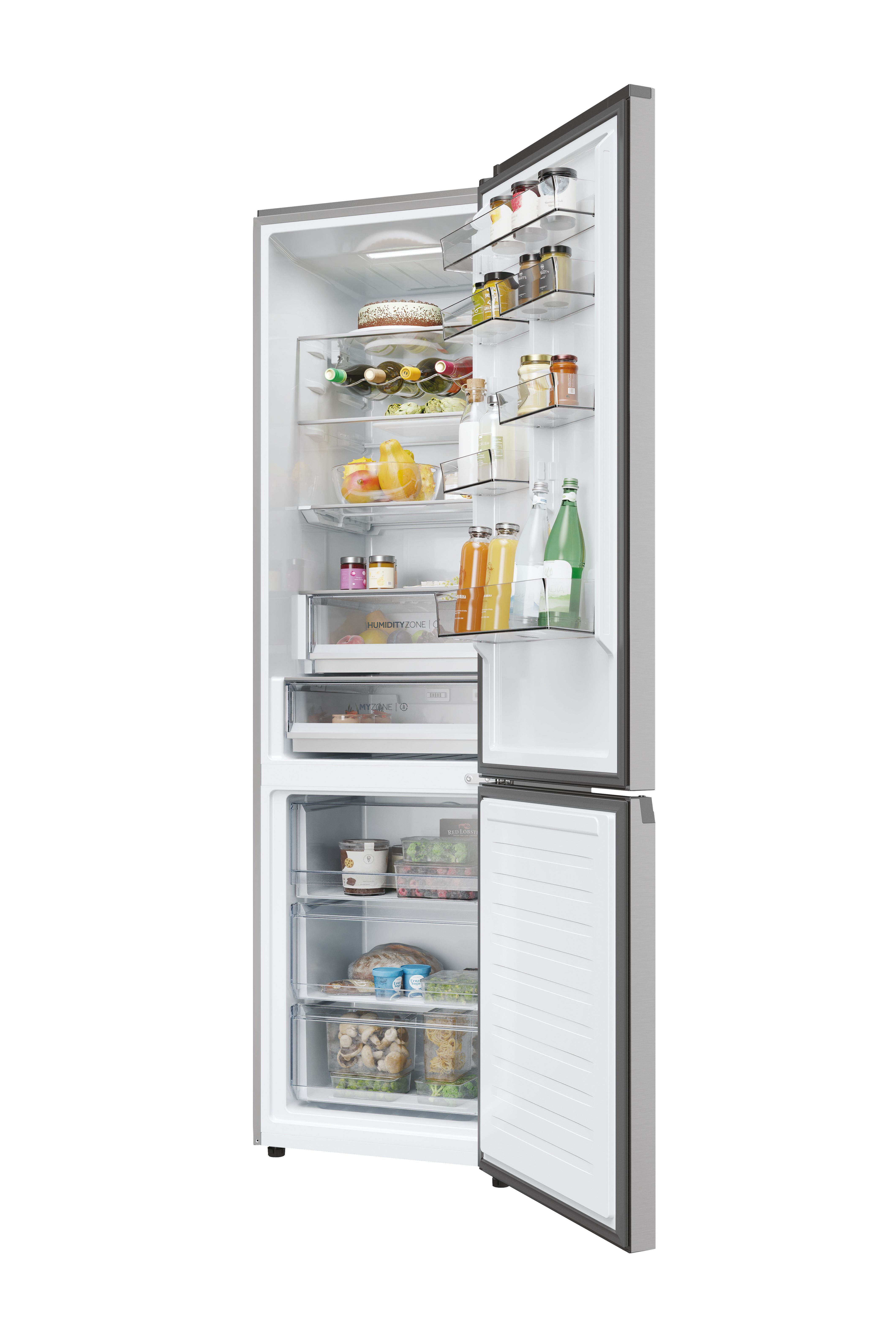 Refrigerador plateado, puertas abiertas, lleno. Estantes superiores: frascos, botellas, pastel. Medio: fruta, zumo. Abajo: cajones, comida.