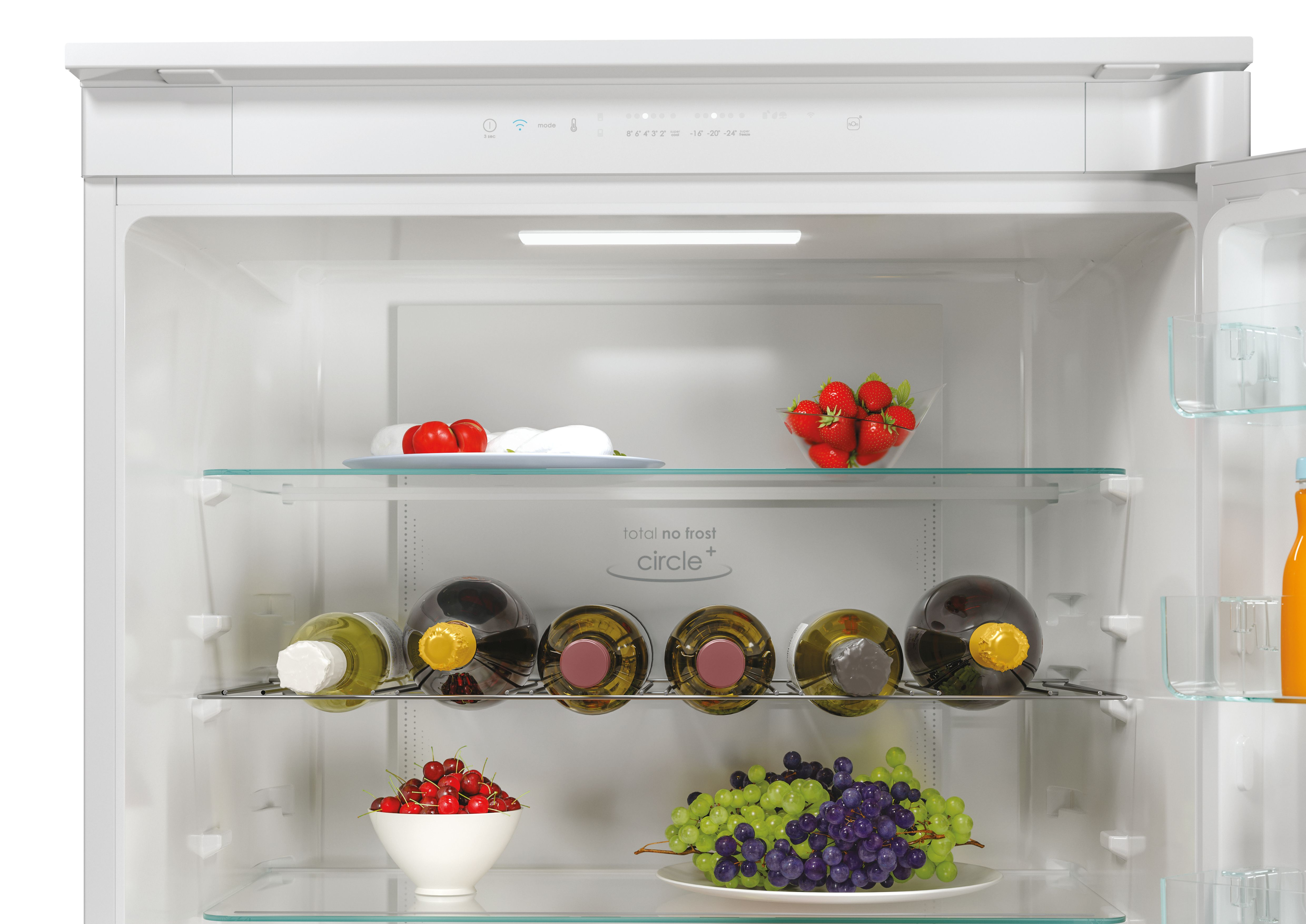 All'interno di un frigorifero bianco. Ci sono ripiani con cibo: fragole, ciliegie, uva e bottiglie di vino.