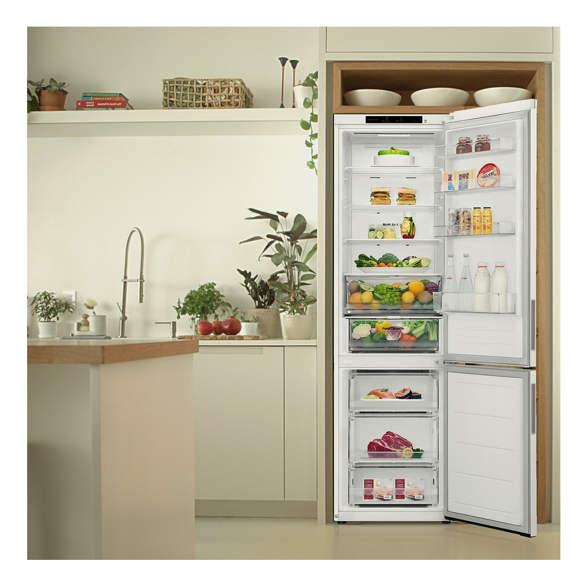 Una cocina con un refrigerador abierto lleno de alimentos, junto a un fregadero, plantas y una encimera de madera.