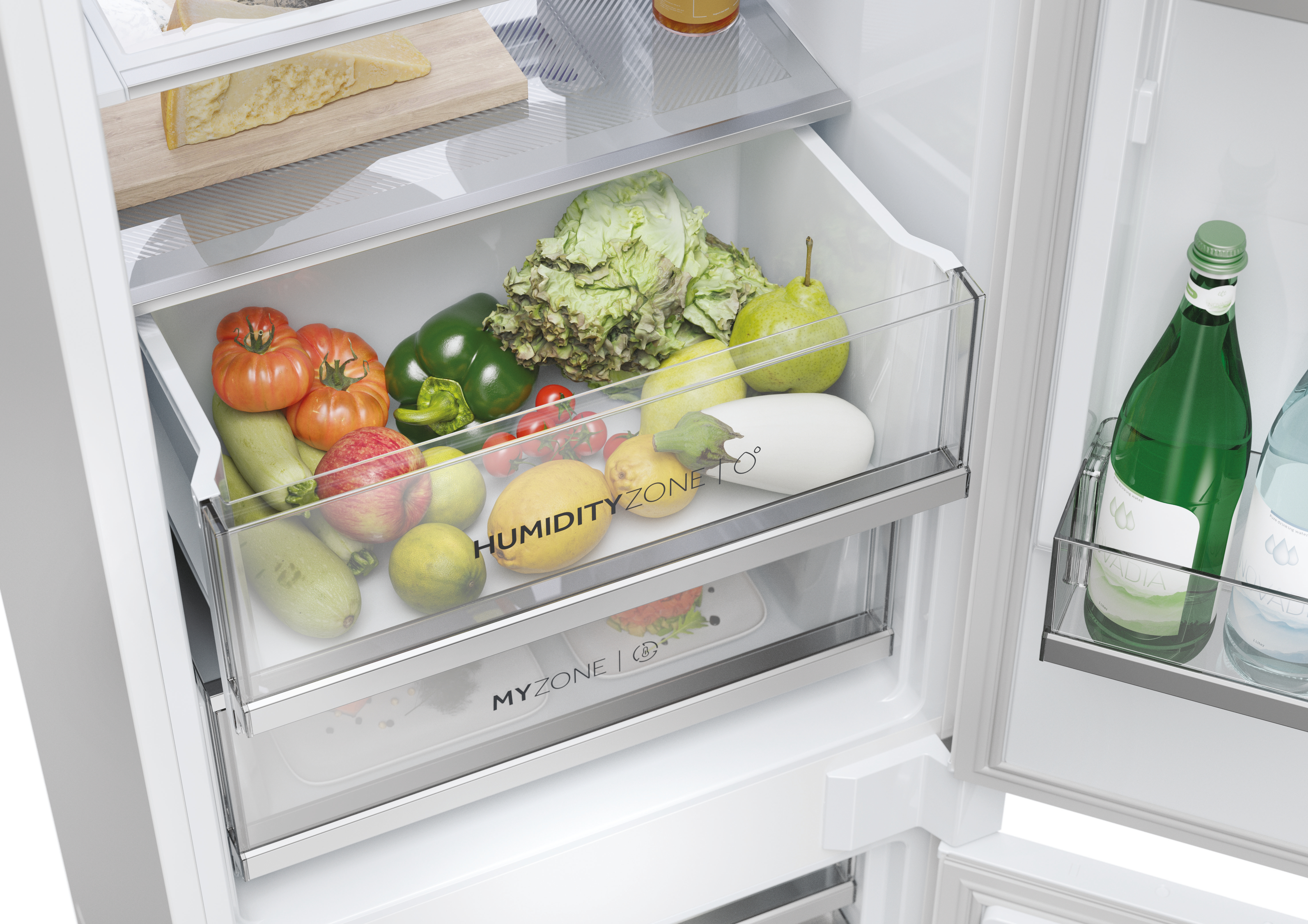 Primer plano de un cajón de refrigerador lleno de productos frescos, incluyendo tomates, y una botella.