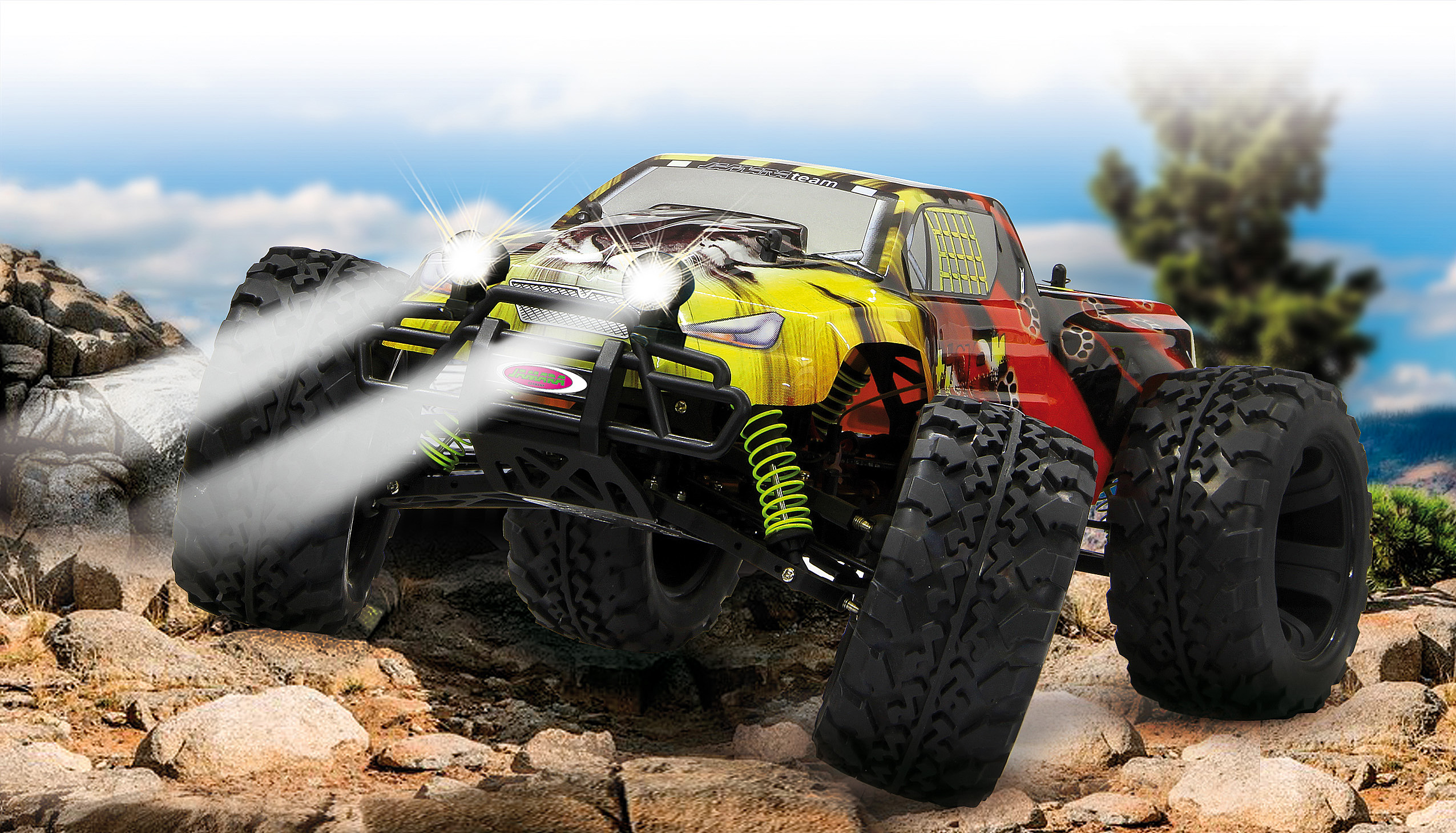 Gelb-roter RC-Truck auf Felsen, Licht an. Szene zeigt Felsen und blauen Himmel im Hintergrund.