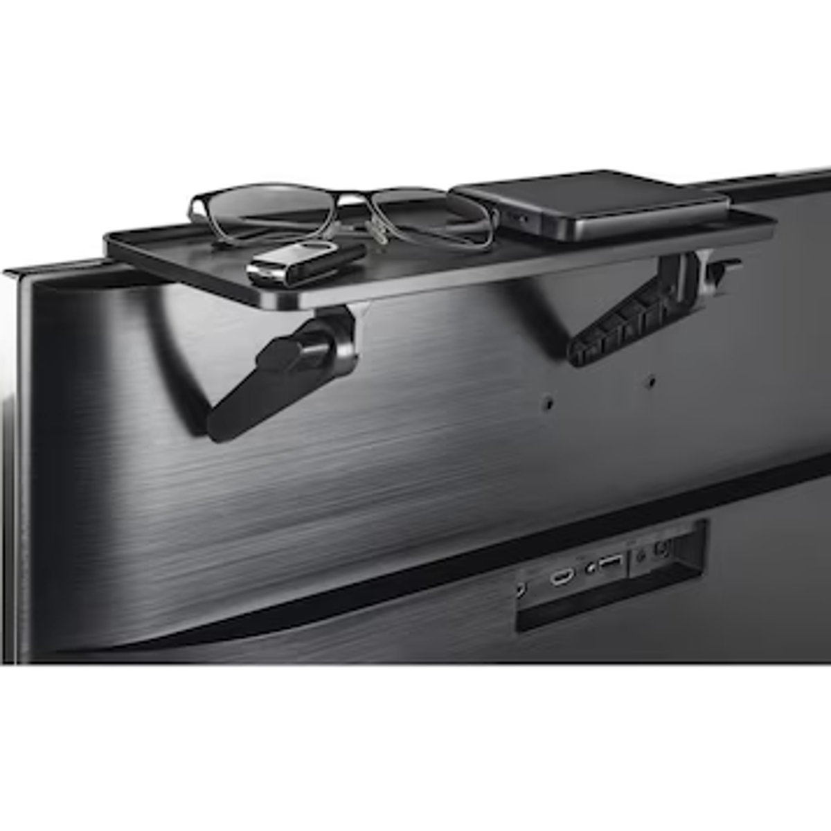 Półka z tyłu telewizora z okularami, pilotem i telefonem.