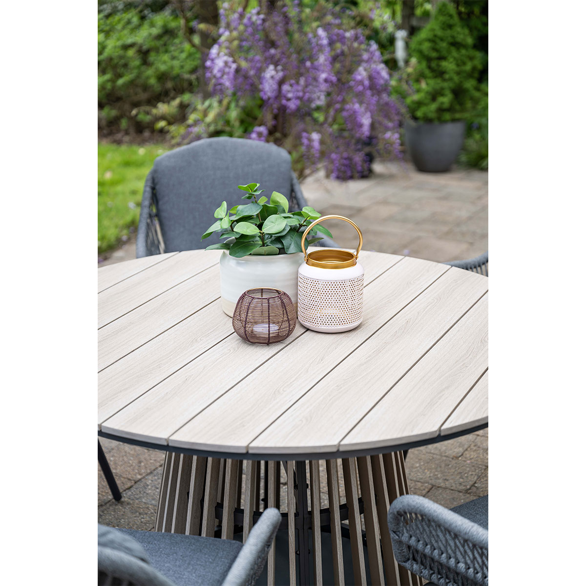 A round table on a patio with decor. A green plant, candle, and a decorative lantern are on the table.