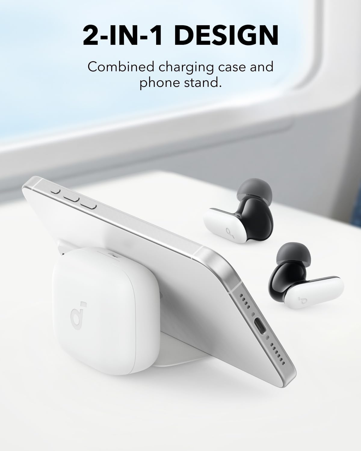 Un teléfono blanco está apoyado en un estuche de carga, con auriculares cerca, sobre una superficie blanca.