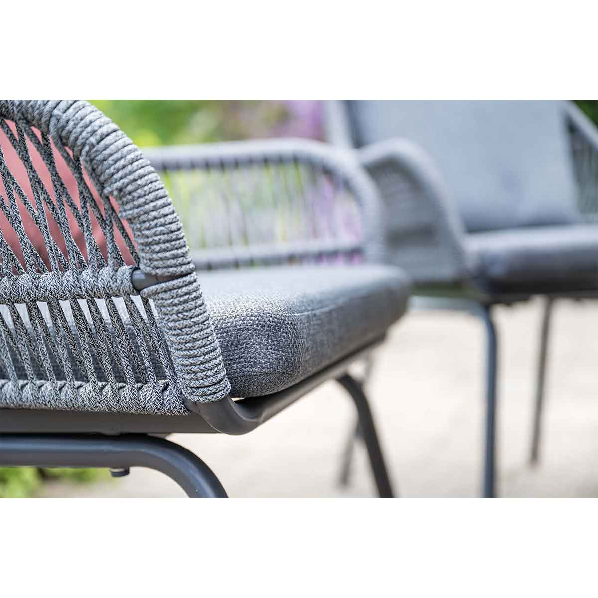 A close-up of a gray woven chair with a gray cushion is shown outdoors.