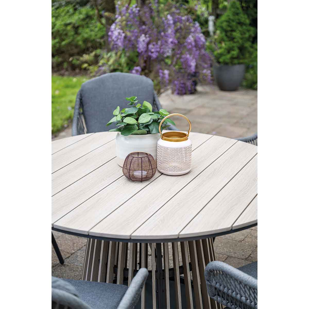 A round outdoor table is decorated with plants and accessories on a stone patio.