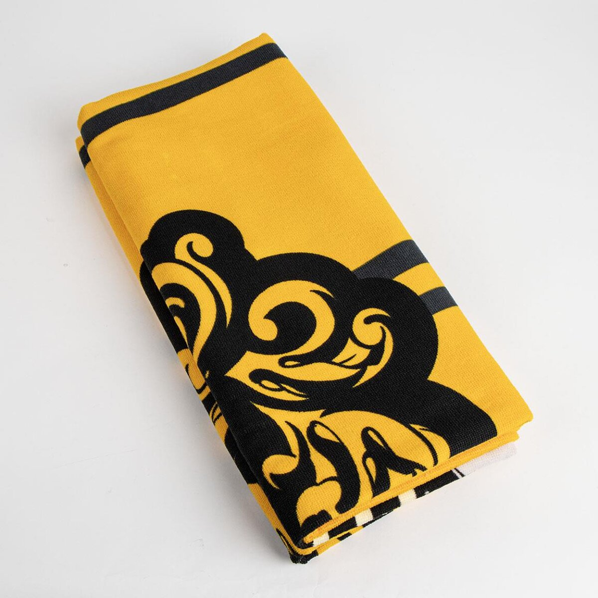 Una toalla amarilla doblada con diseño floral negro. Sobre una superficie blanca.