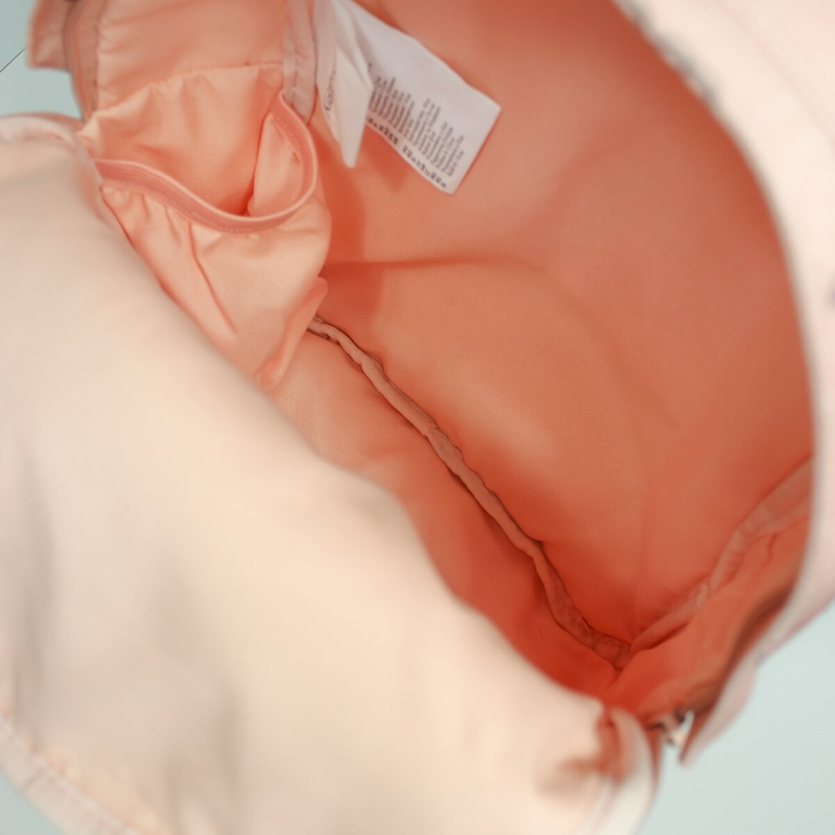 Binnenkant van een roze rugzak. Het heeft een perzikkleurig interieur met een klein zakje en een label.