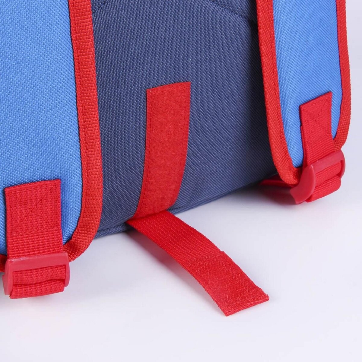Primer plano de una mochila azul y roja con correas y hebillas rojas. La mochila está sobre un fondo blanco.