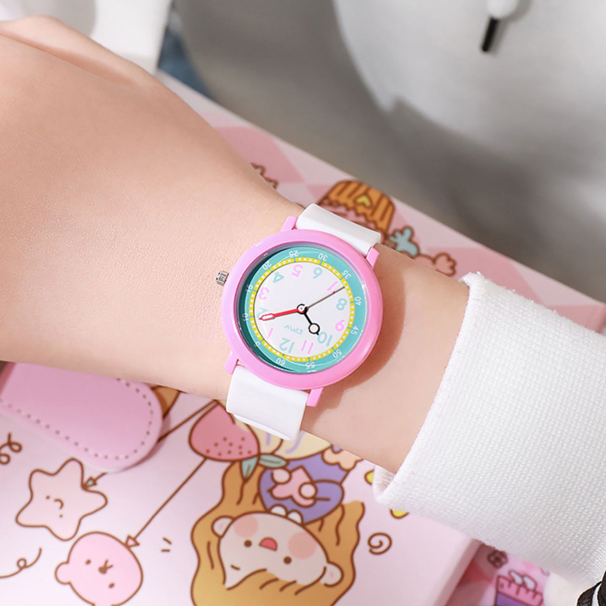 Handgelenk einer Person mit einer Uhr mit rosa Rahmen und weißem Armband. Das Zifferblatt ist rosa, weiß und grün.