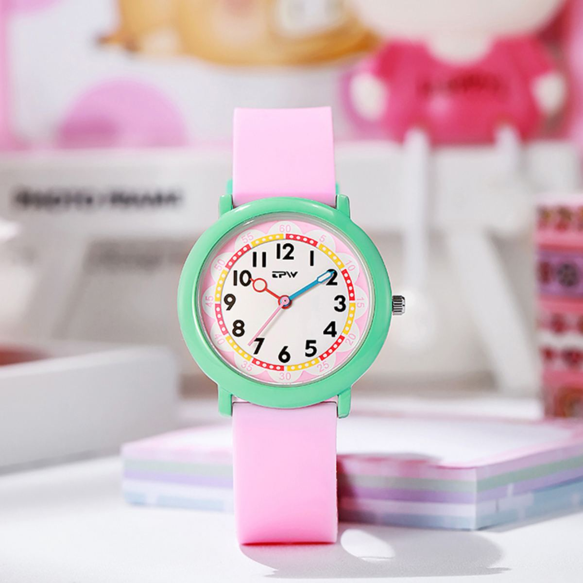Orologio rosa con lunetta verde. L'orologio è su uno sfondo rosa.