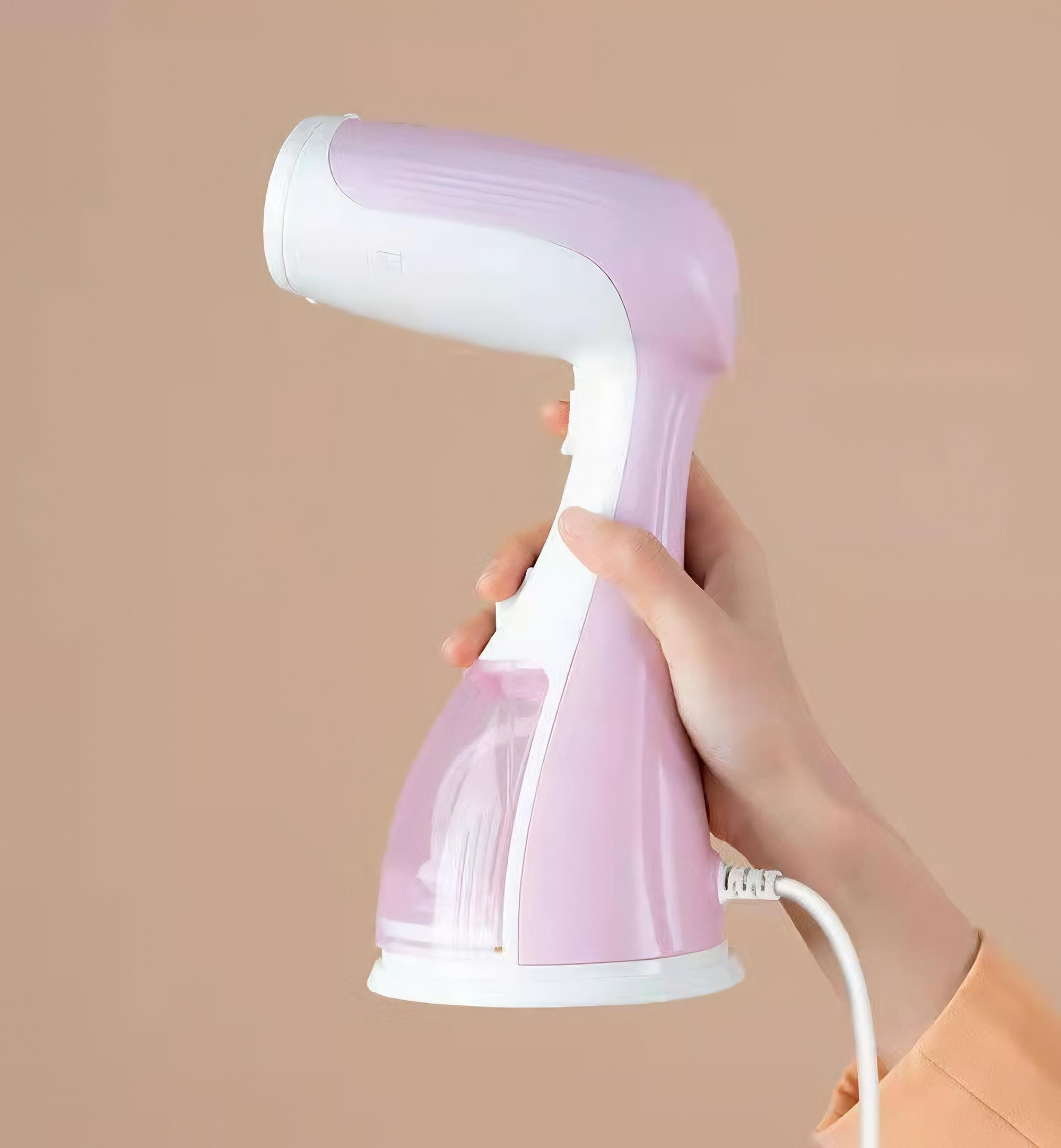 Ein rosa-weißes Hand-Dampfbügeleisen. Eine Hand hält das Gerät. Ein Netzkabel ist angebracht.