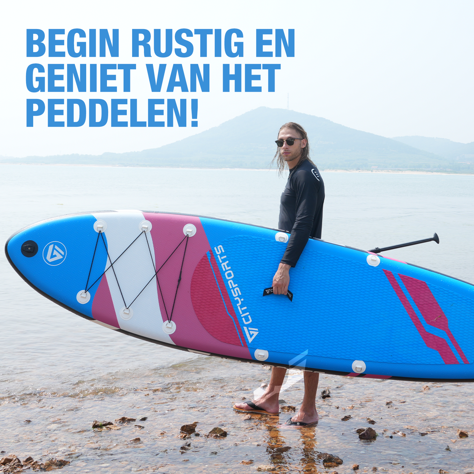 Un homme sur une planche à pagaie sur un lac, avec une montagne en arrière-plan. La planche est bleue et rose.