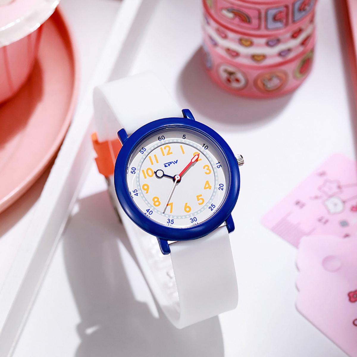 Un reloj blanco con bisel azul, que muestra la hora. El reloj está sobre una bandeja con otros objetos.