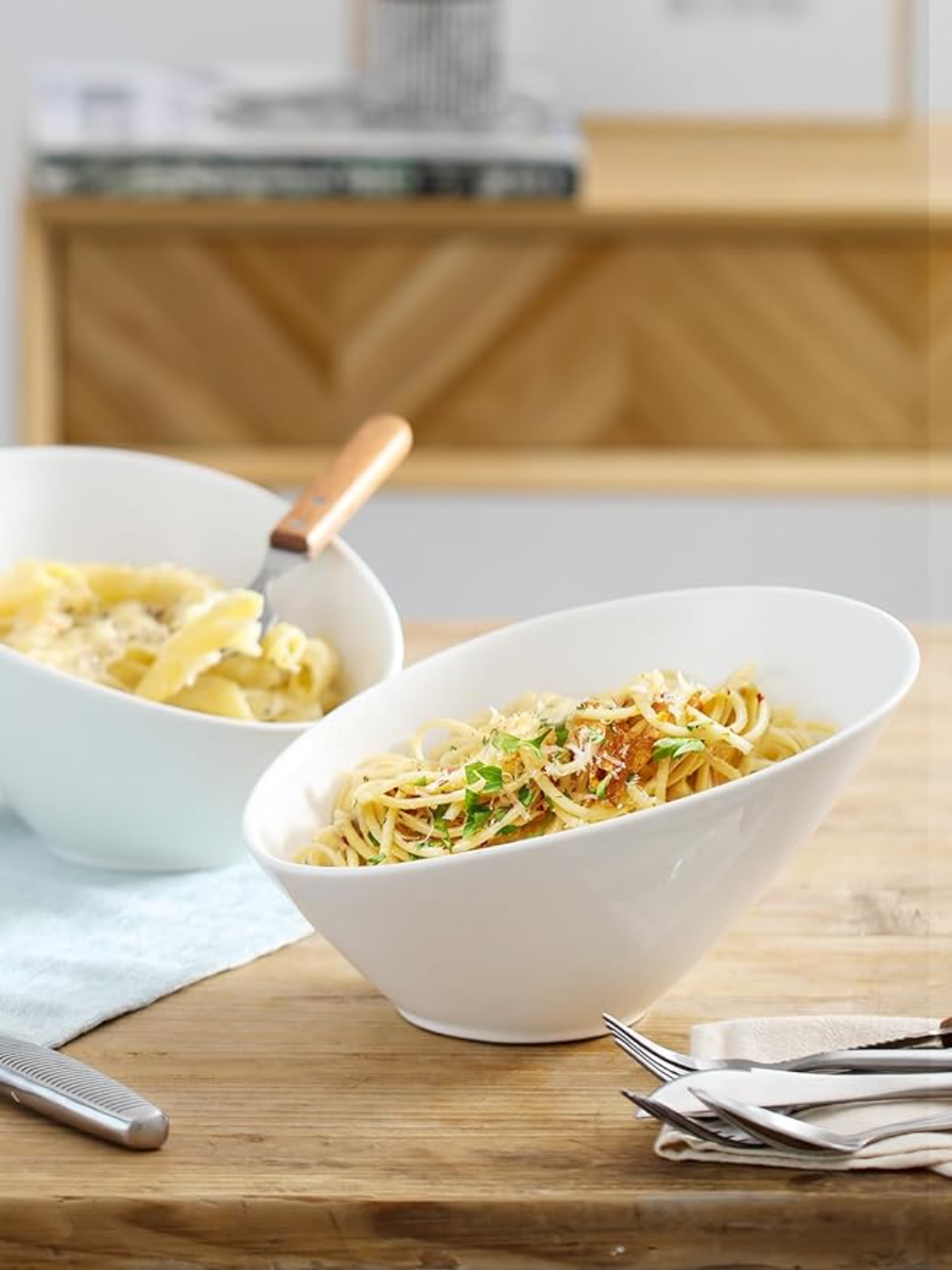 Zwei weiße Schalen mit Spaghetti und Käse. Eine Schüssel hat Nudeln mit einer Gabel darin.