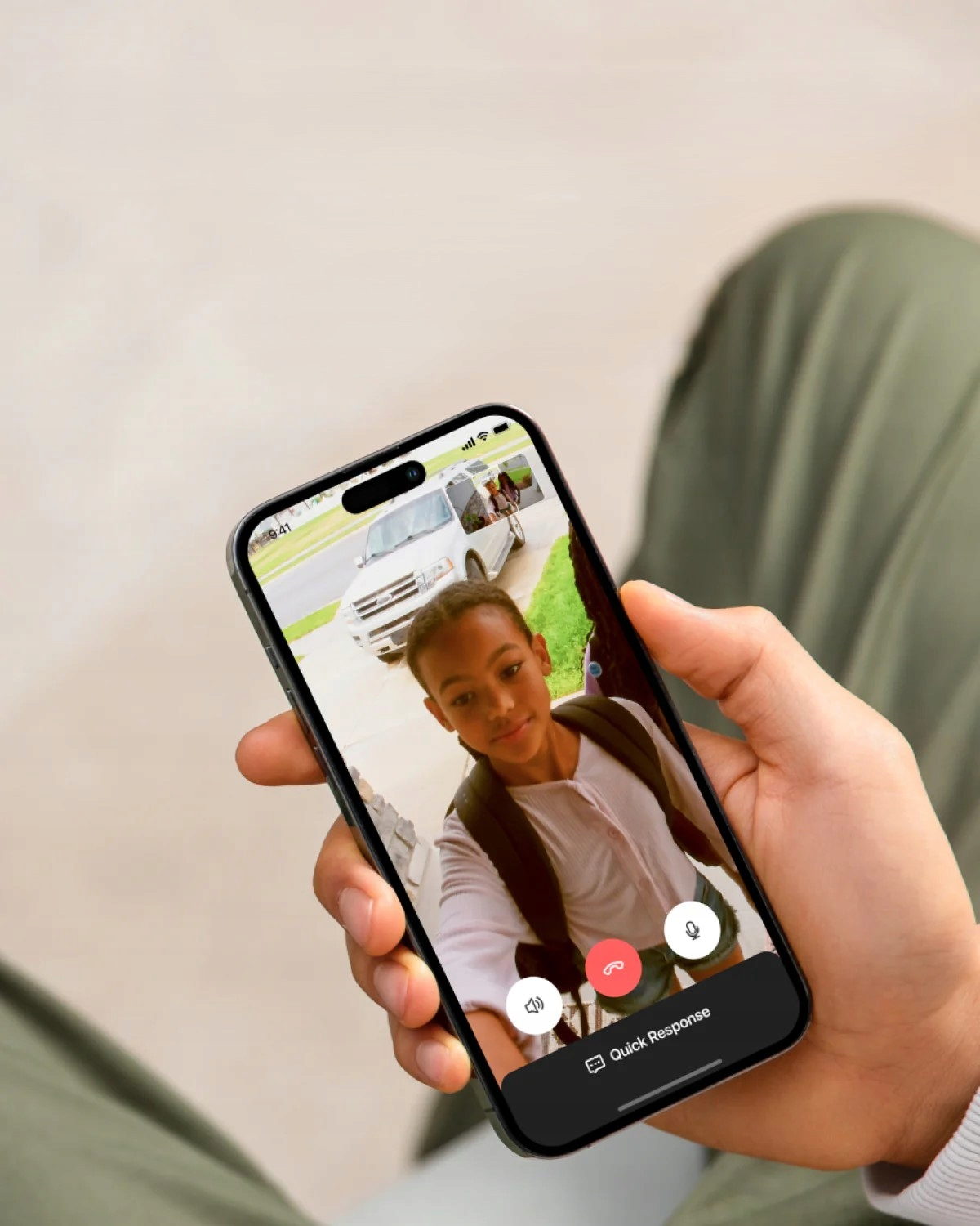 Osoba trzyma telefon z podglądem na żywo chłopca, z samochodem w tle.