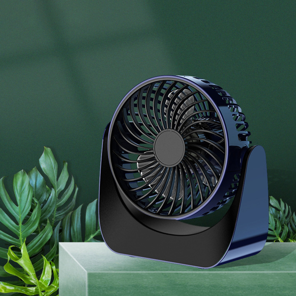 Ein dunkelblauer Ventilator auf dunklem Sockel, mit schwarzen Flügeln. Er hat ein geschwungenes Design und steht auf grüner Oberfläche.