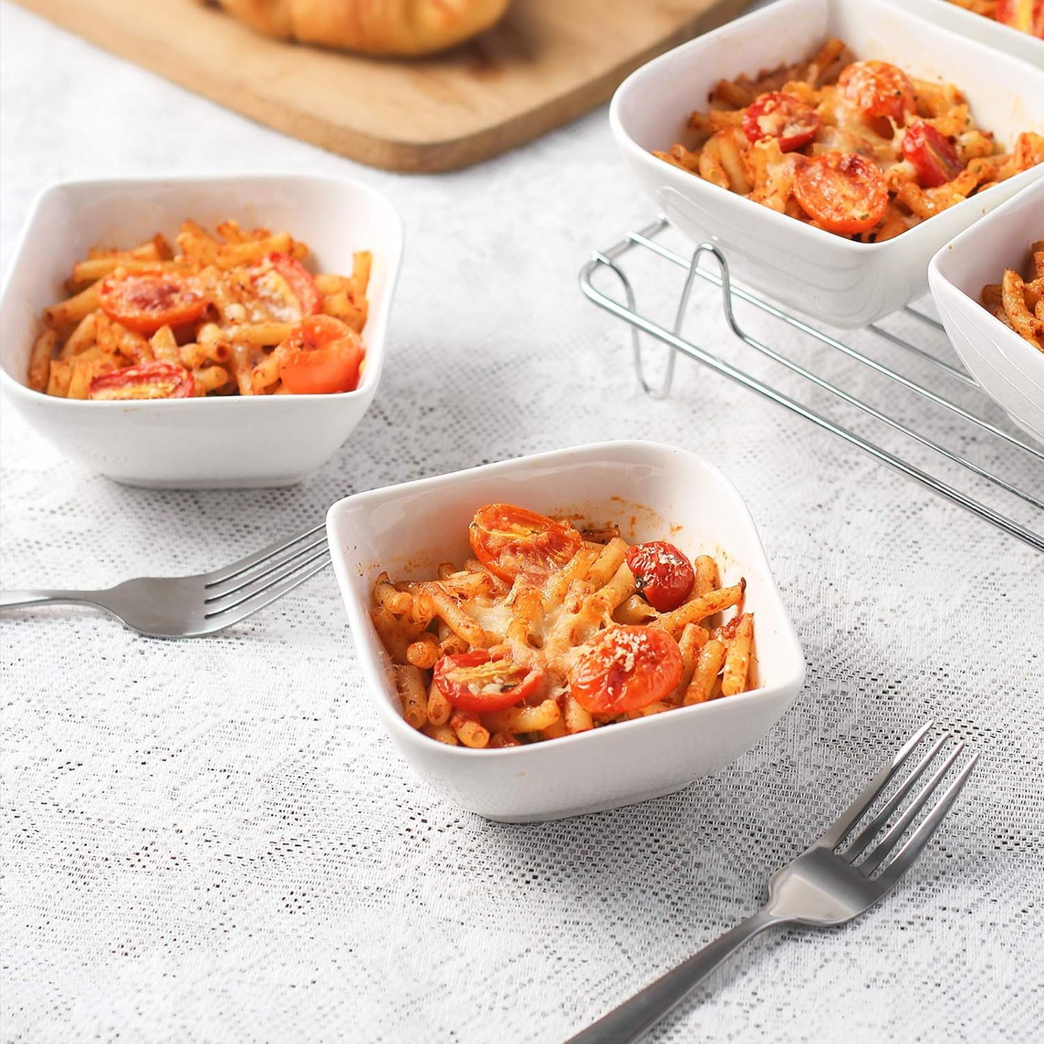 Piatti bianchi quadrati con pasta e pomodori. Forchette sulla tovaglia bianca di pizzo. Tavola di legno sullo sfondo.