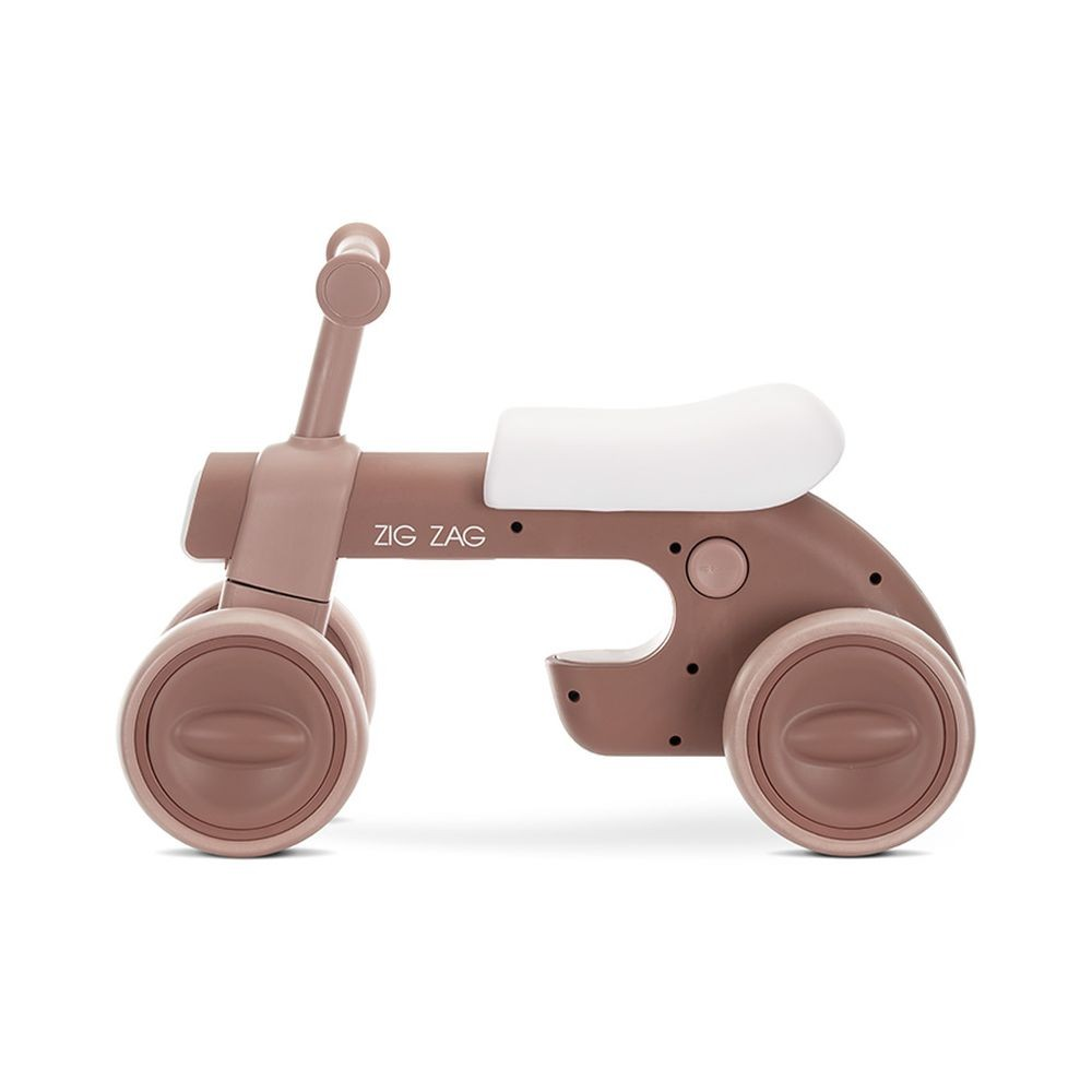 Una bicicleta de equilibrio rosa y blanca para bebés con cuatro ruedas. Tiene 'ZIG ZAG'.