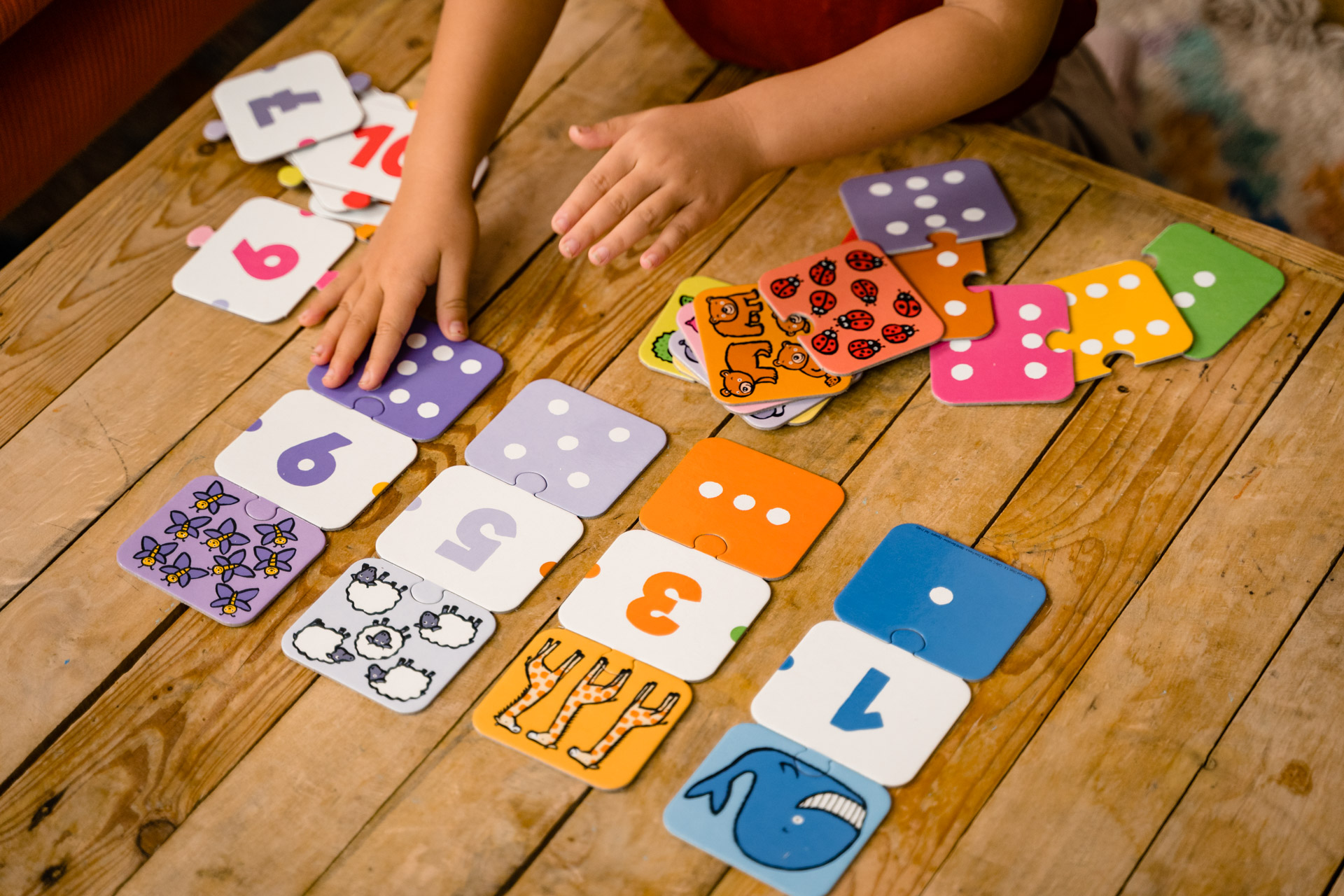 Die Hand eines Kindes ordnet Zahlen-Zuordnungsspielkarten auf einem Holztisch an.