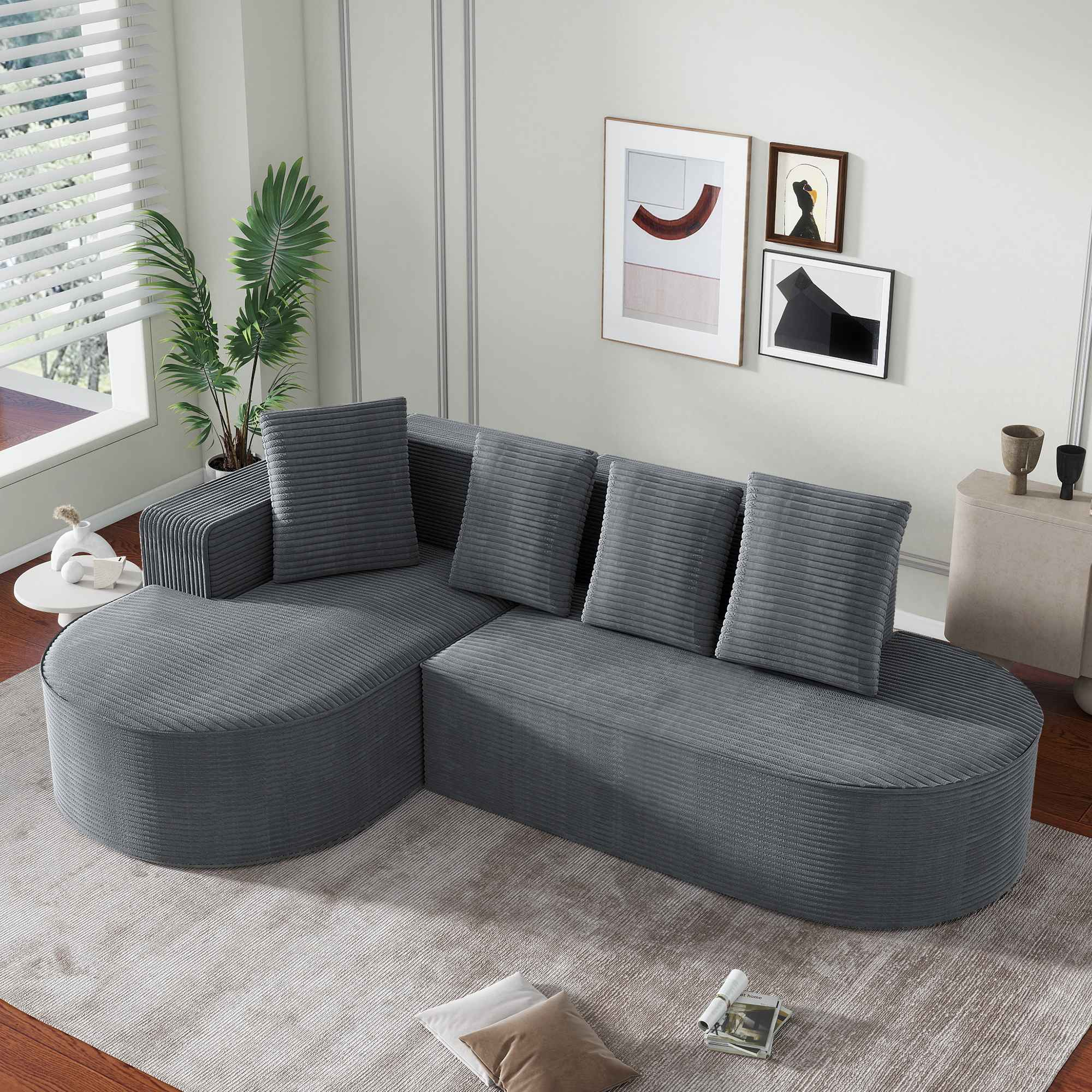 Graues Cordsofa mit Chaiselongue, Zierkissen und einer Pflanze in der Nähe eines Fensters.