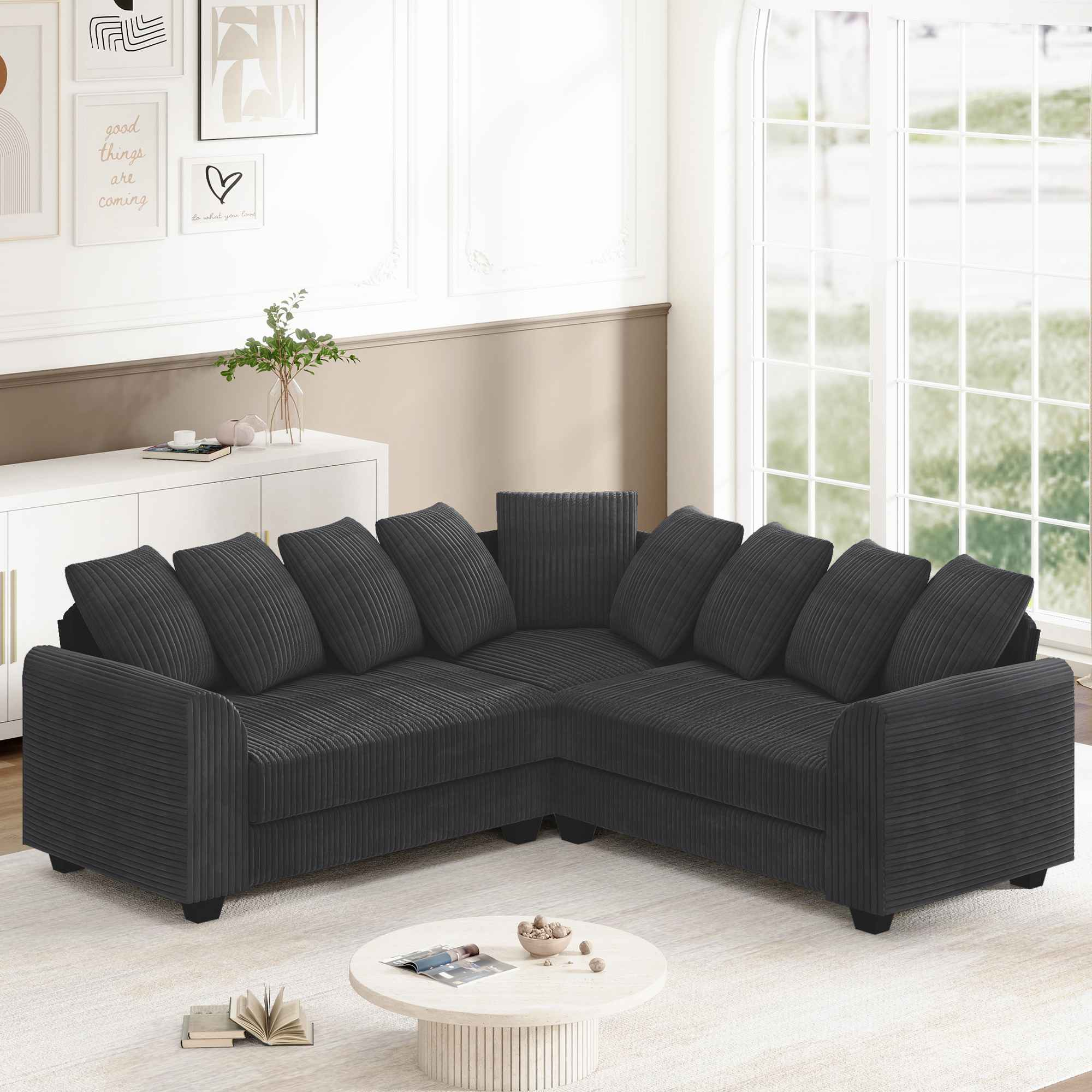 Ein dunkelgraues Ecksofa in einem Raum mit weißer Wand, Fenster und Kunst. Davor steht ein runder Tisch.