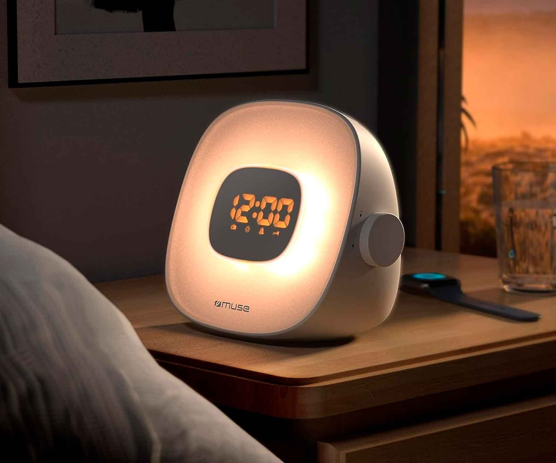 Una lámpara de noche blanca que muestra la hora 12:00. La habitación está oscura, con una cama y una ventana al fondo.