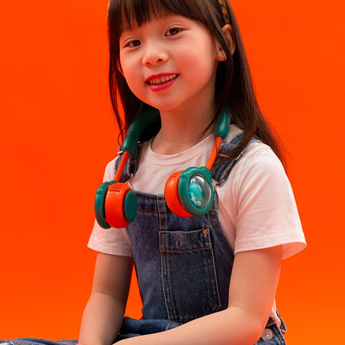 Ein junges Mädchen mit einem Nackenventilator. Der Hintergrund ist orange.