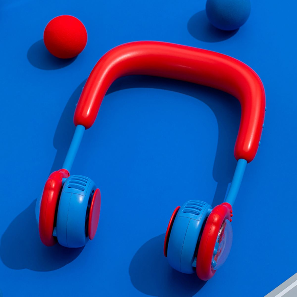 Roter und blauer Nackenventilator auf blauer Oberfläche mit zwei blauen und einem roten Ball.