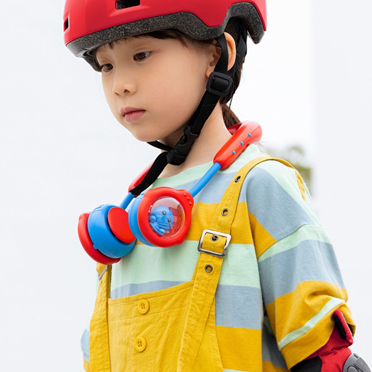 Kind mit Helm und Nackenventilator, gelb und blau, im Freien.