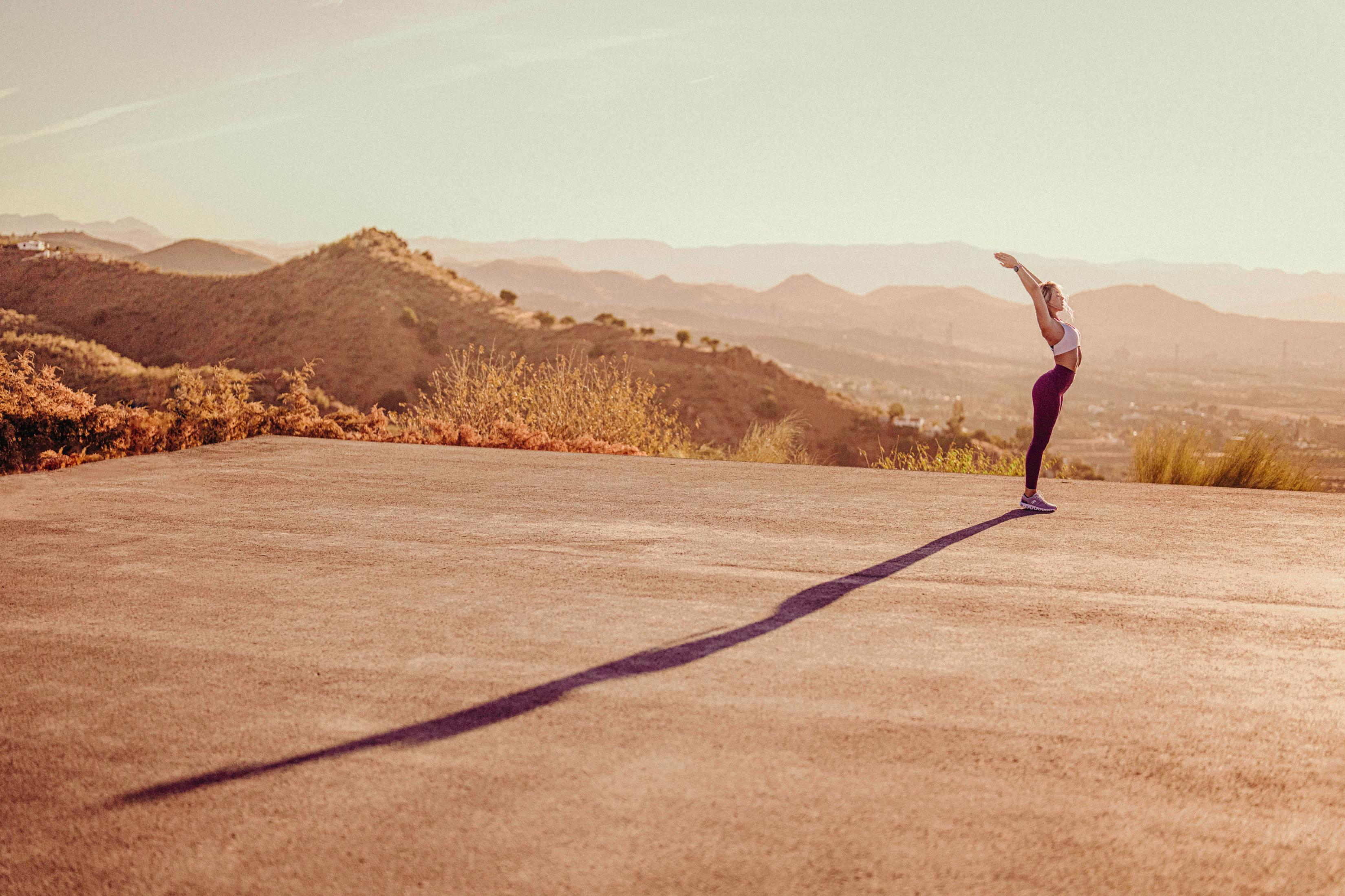 Kobieta w stroju sportowym rozciągająca się na zewnątrz, z krajobrazem w tle.