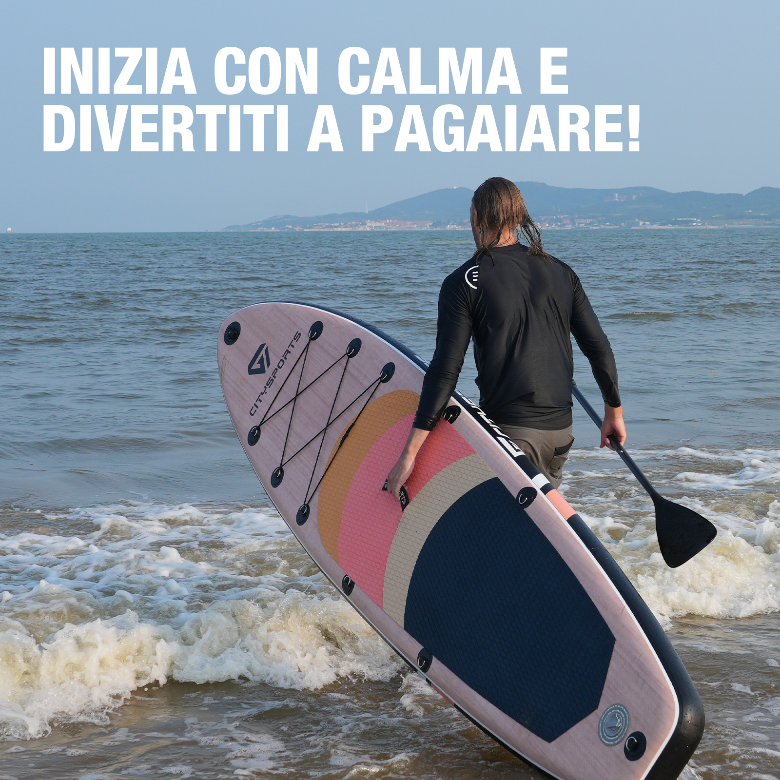Una persona che porta una tavola da paddle verso il mare. La tavola è rosa e ha un design colorato.