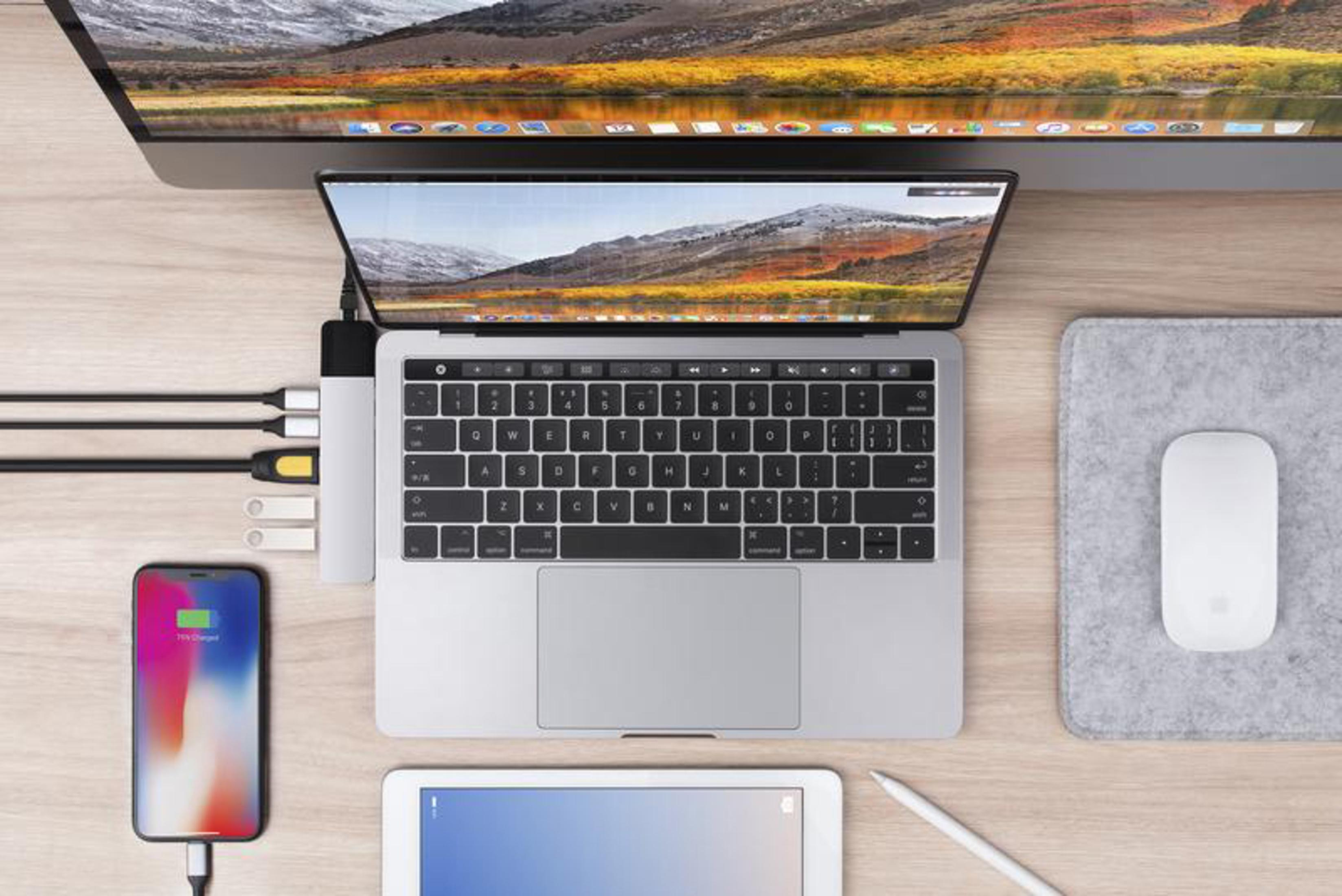 Configurazione laptop con telefono, tablet, hub USB e monitor, su una scrivania di legno.