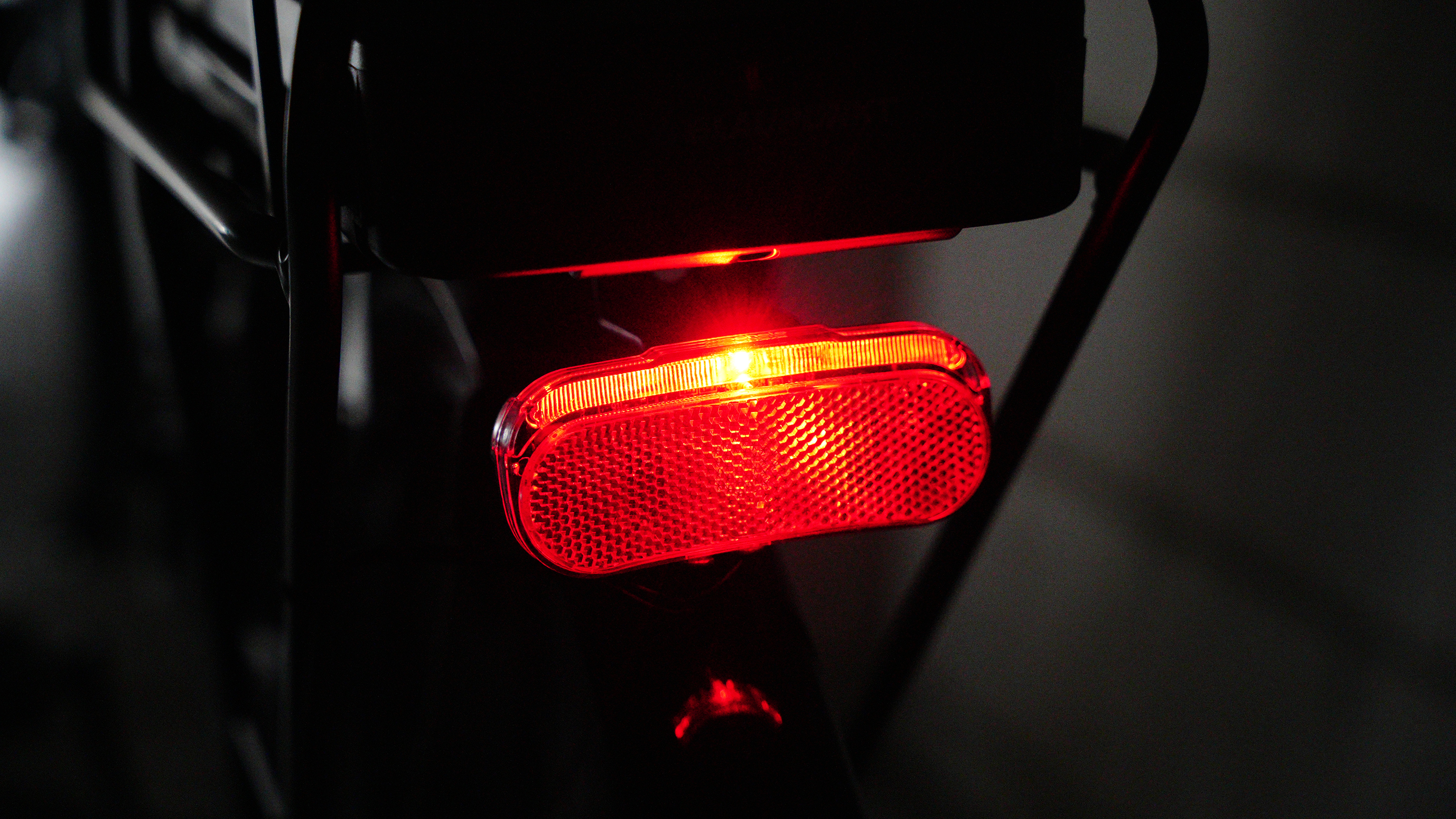 Nahaufnahme eines roten Rückstrahlers an einem Fahrrad, beleuchtet durch Licht.