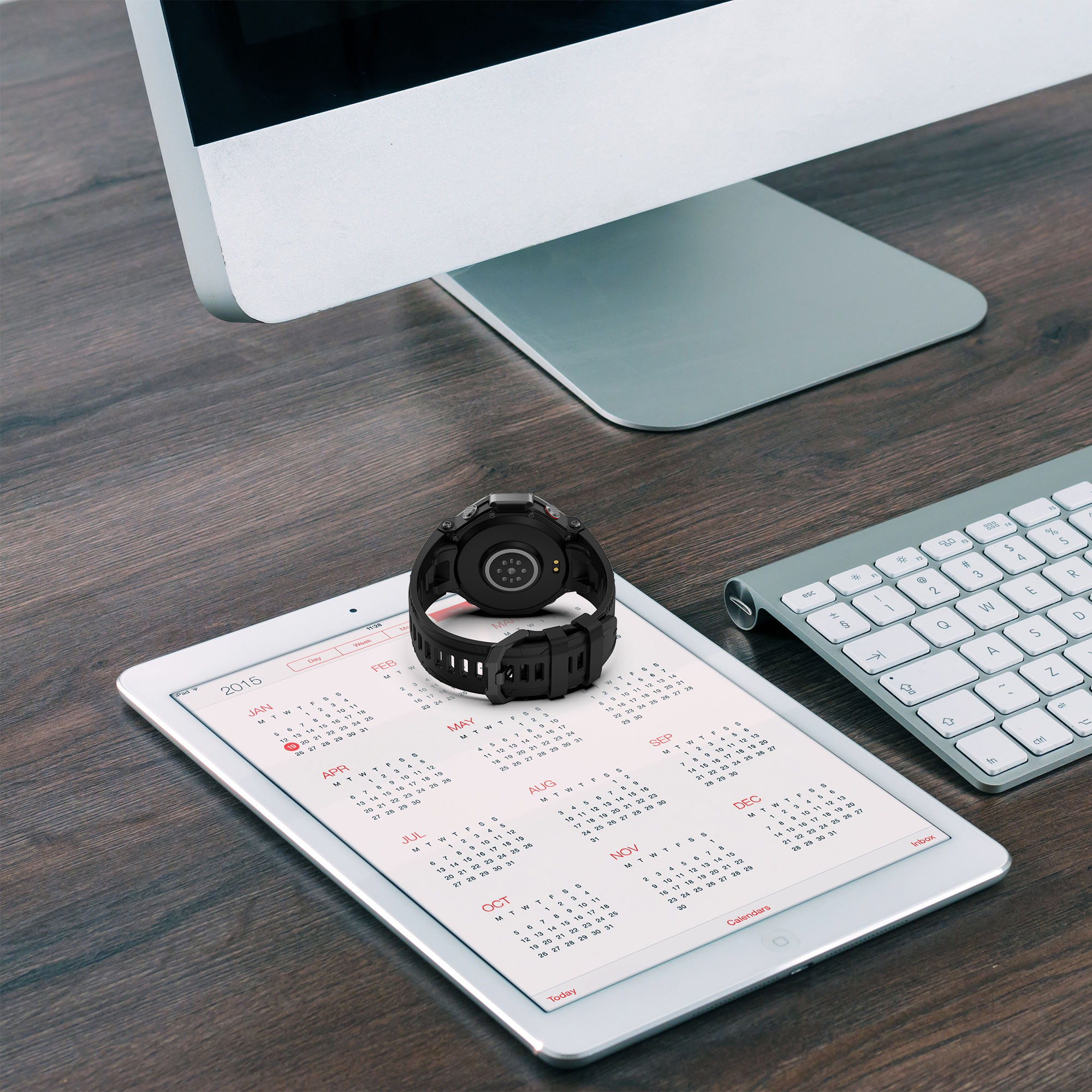 Smartwatch na tablecie kalendarza, klawiaturze i monitorze. Zegarek jest czarny.