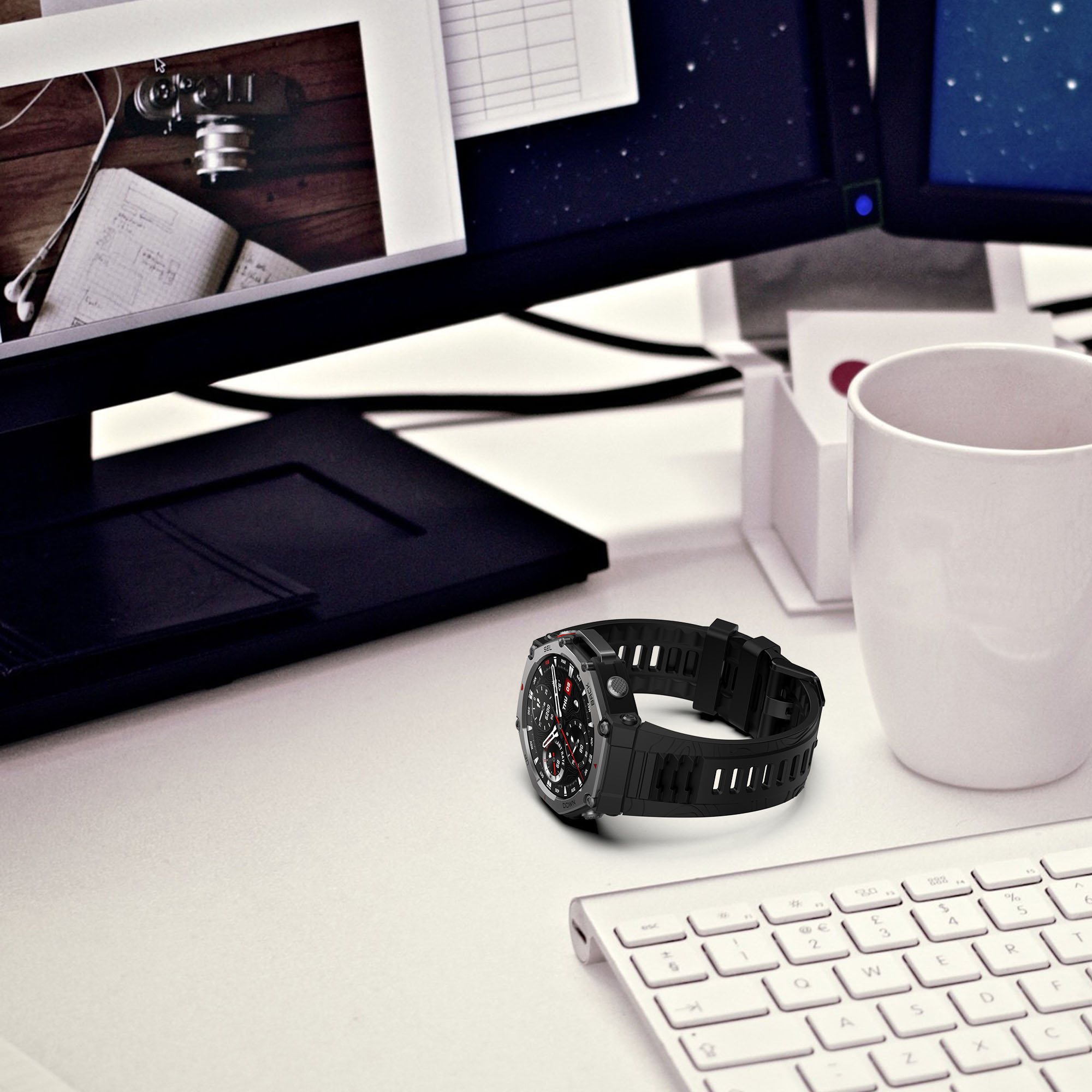 Czarny smartwatch na białym biurku. Klawiatura, notatnik i monitory komputerowe w tle.