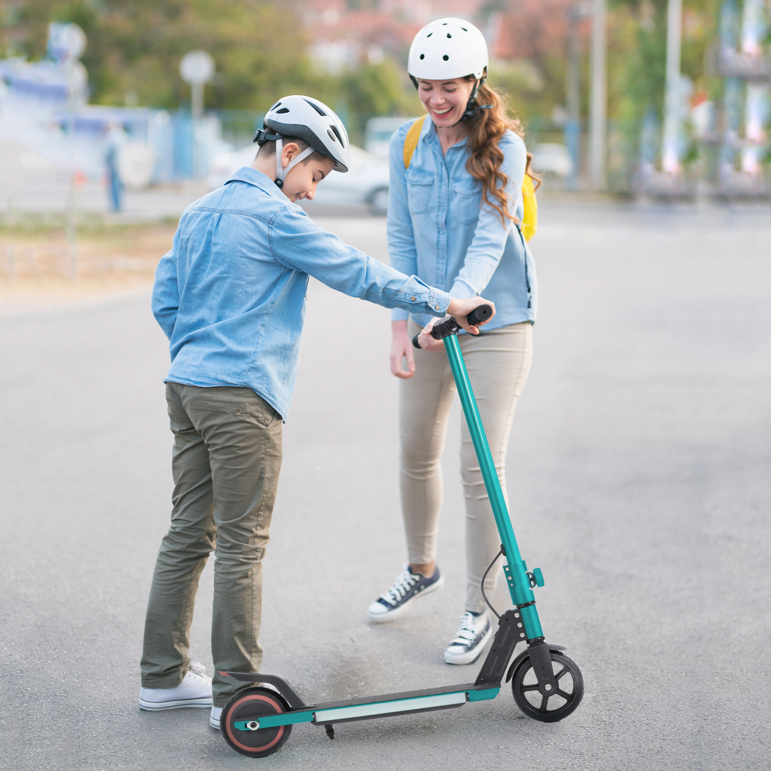 Ein Junge auf einem Roller, gefolgt von einem Mann auf einem Roller. Beide sind im Freien, Bäume im Hintergrund.