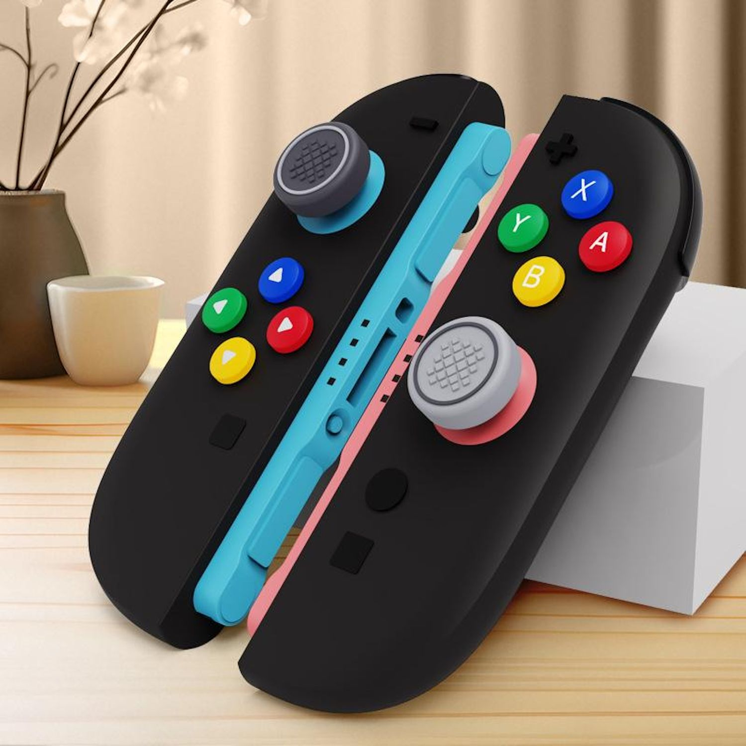 Dos controladores negros con botones coloridos se muestran contra un fondo neutro con elementos decorativos.
