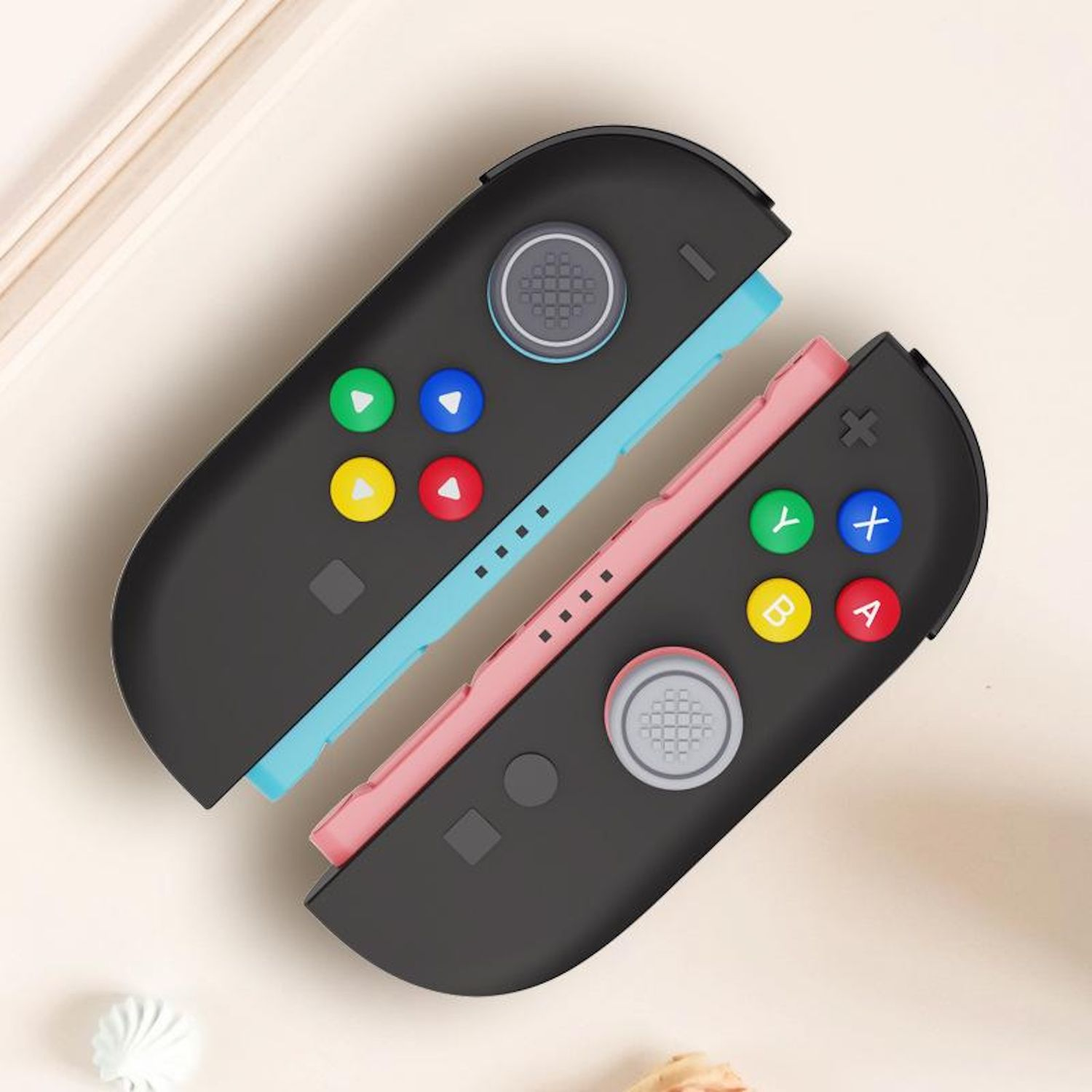 Dos controladores de consola negros con botones coloridos se muestran sobre una superficie clara con elementos decorativos.