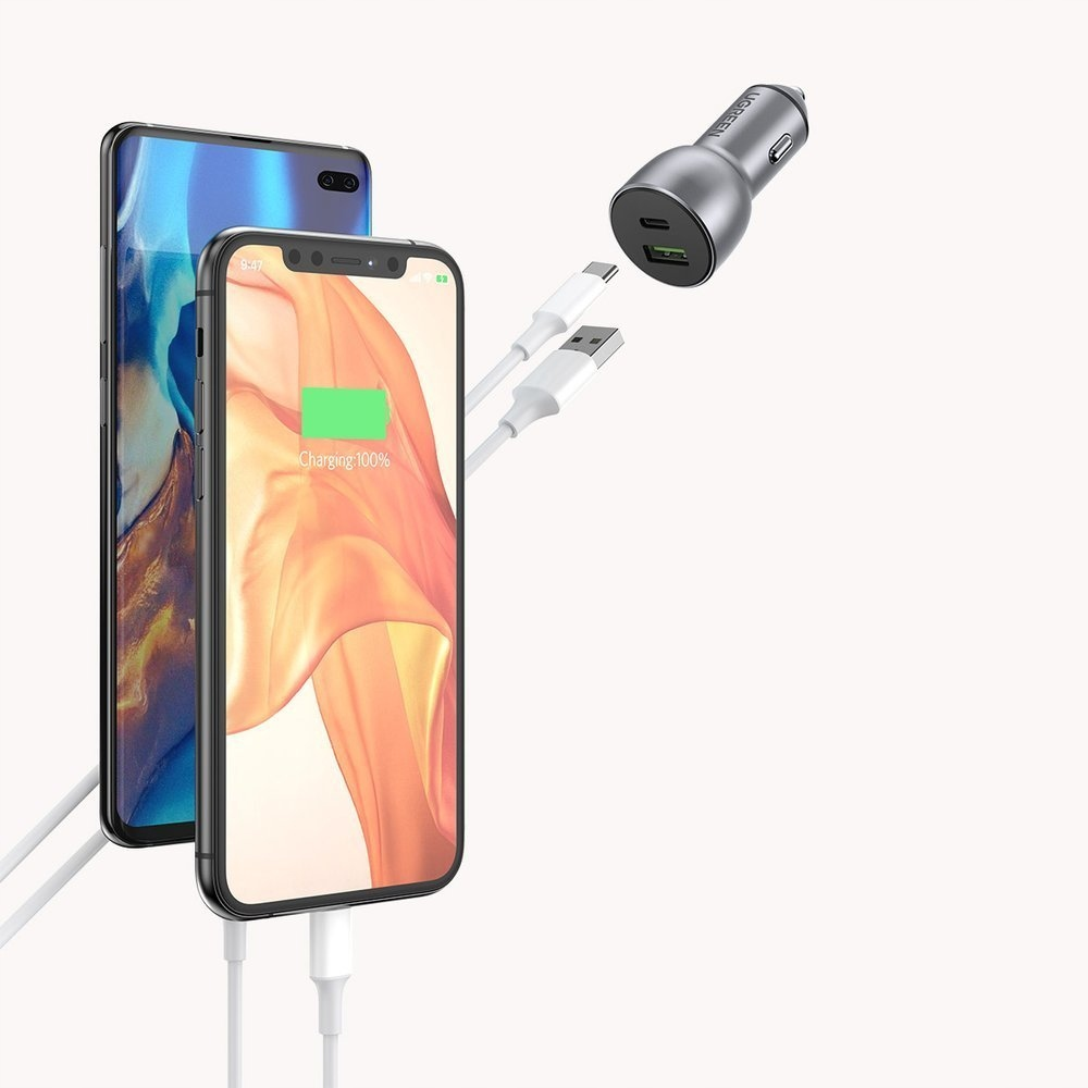 Dwa smartfony ładujące się białymi kablami i ładowarka samochodowa z portami USB w tle.