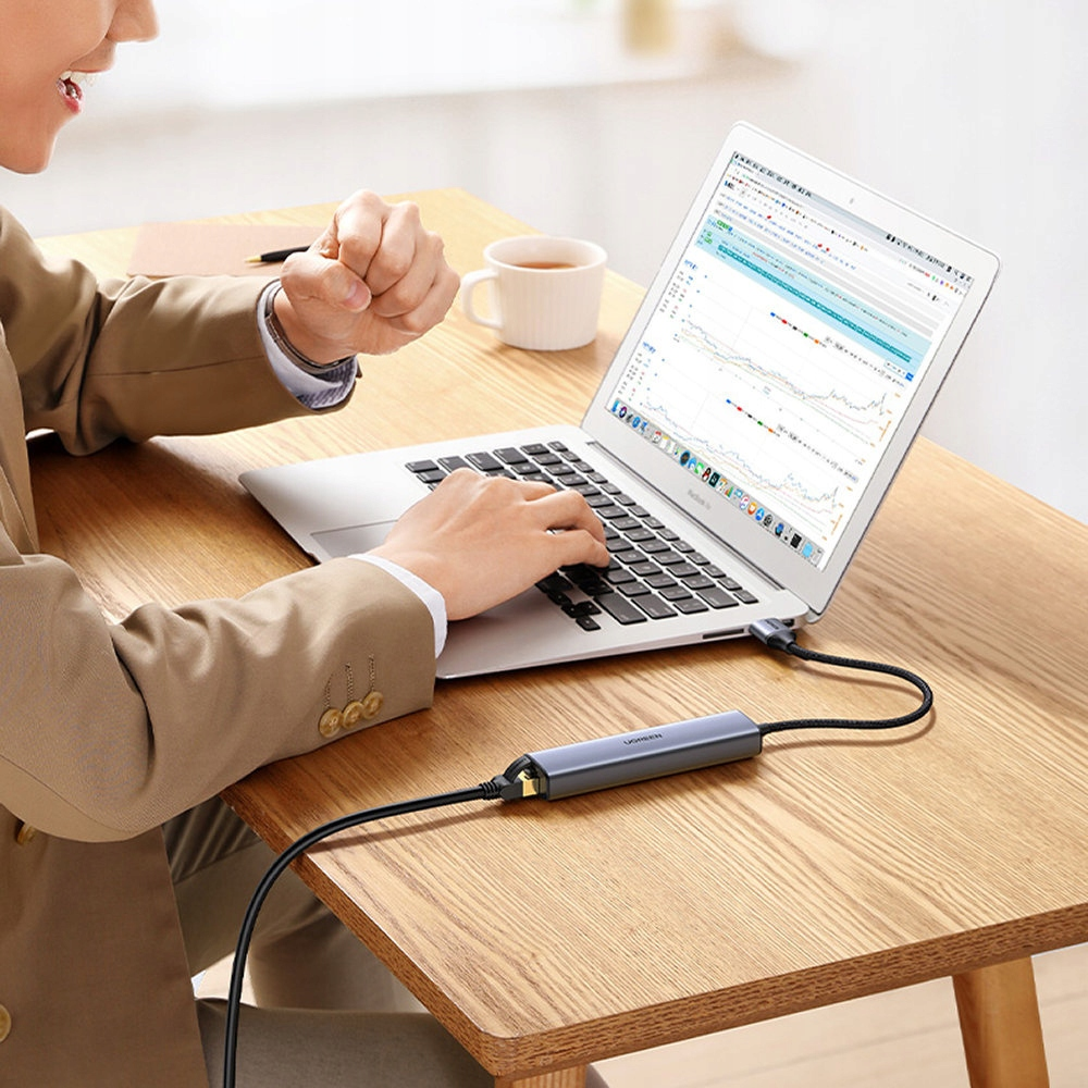 Osoba korzystająca z laptopa podłączonego do koncentratora USB. Ekran laptopa wyświetla wykresy i dane.