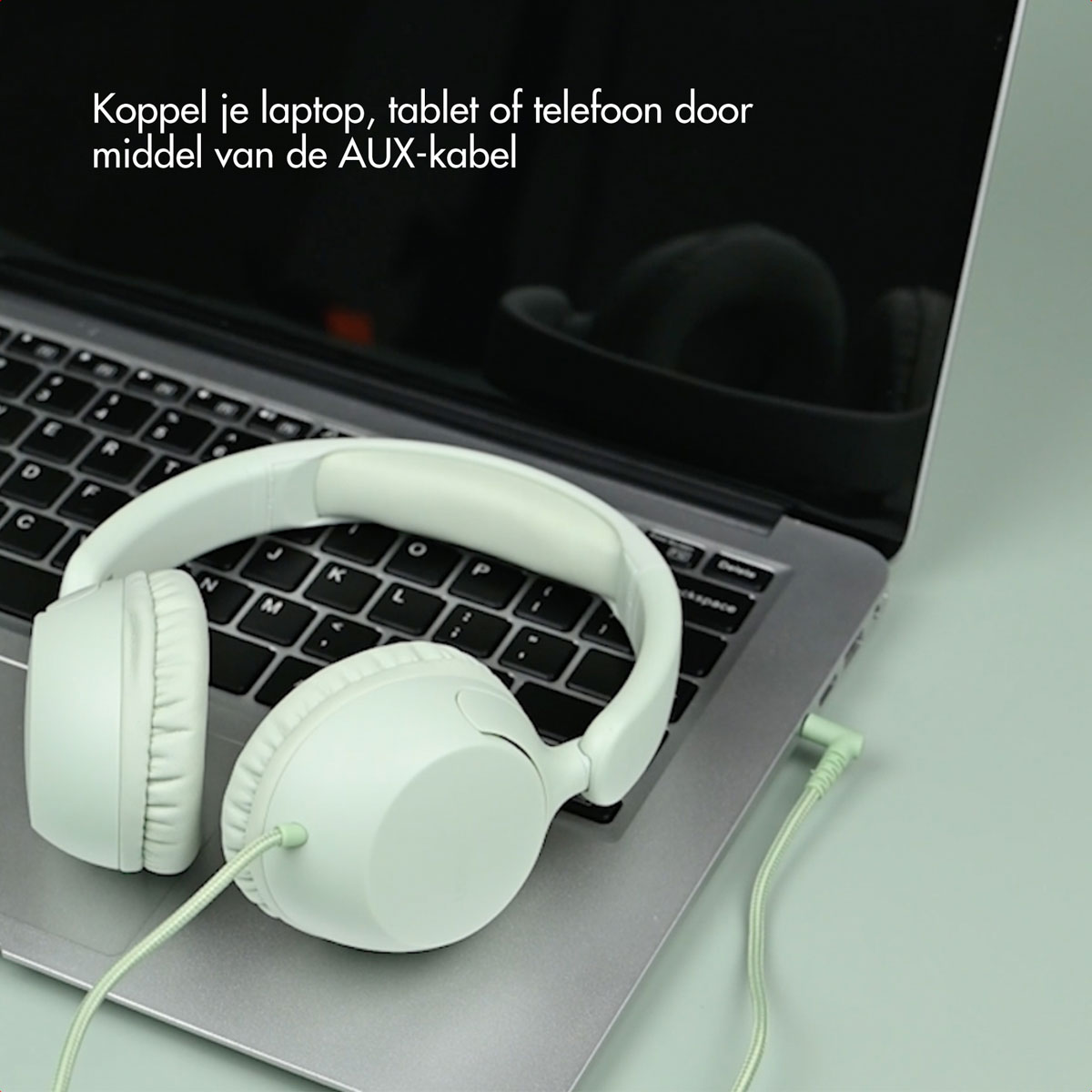 Groene koptelefoon verbonden met een laptop via een AUX-kabel. De laptop staat open op een groen oppervlak.